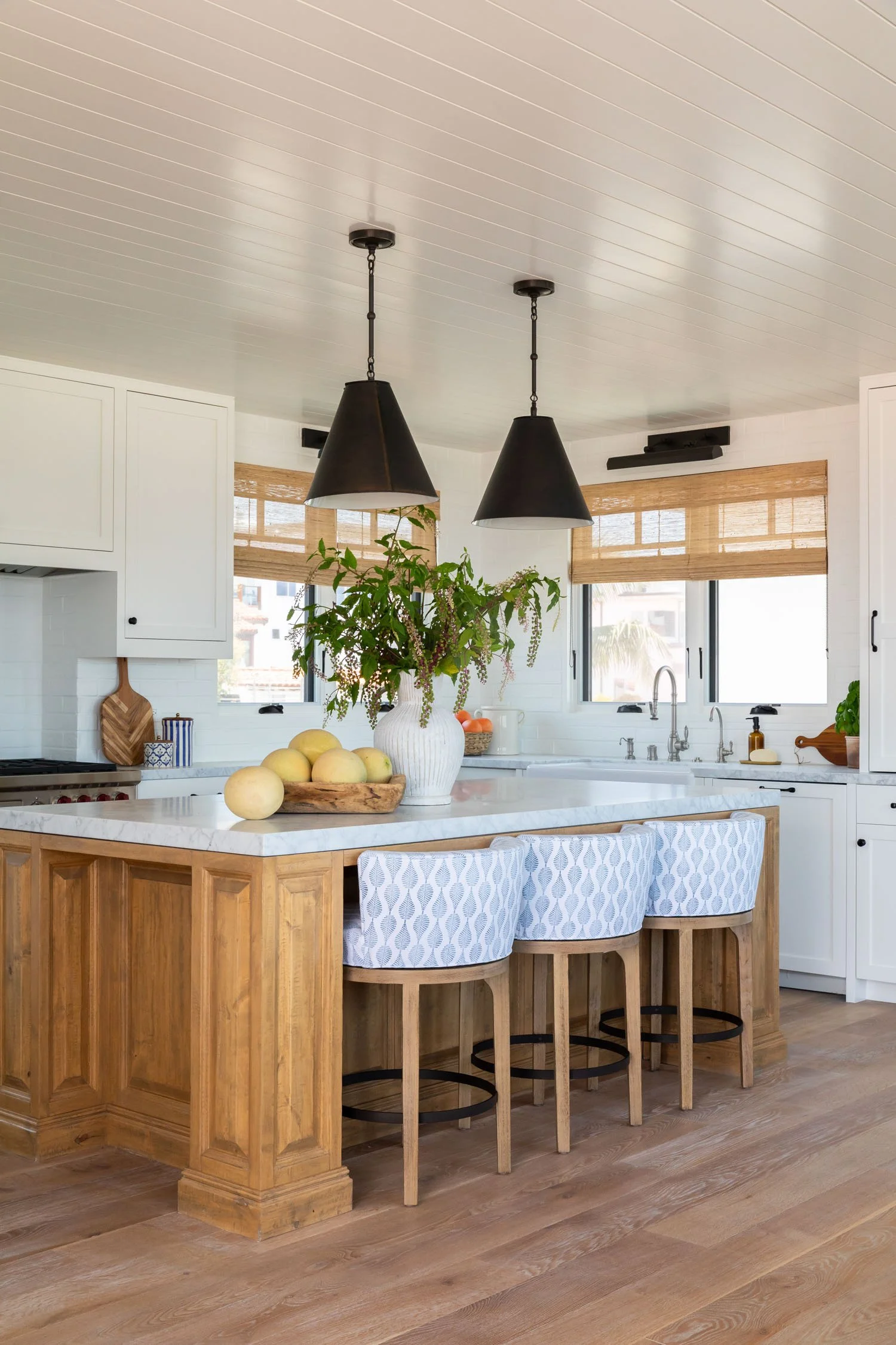 Manhattan Beach kitchen with wood island, patterned counter stools, white cabinetry, and marble countertops by JKB Home Design