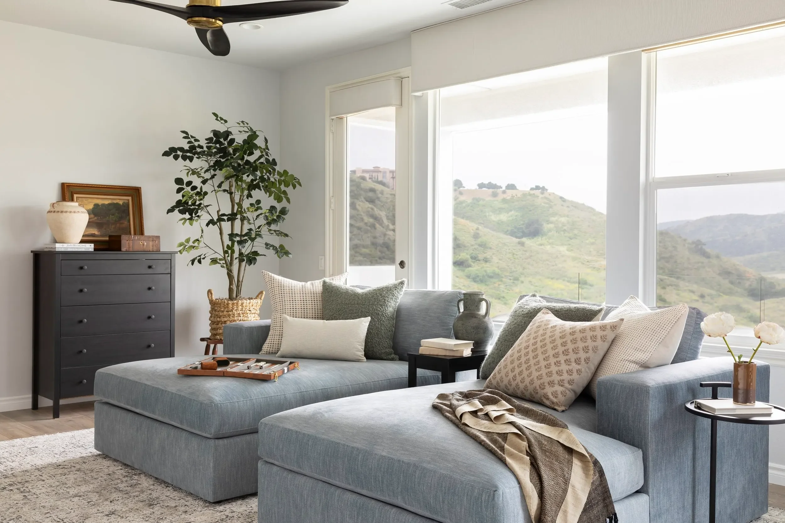 Light-filled living room with blue chaise seating, layered textiles, and hillside views, designed by Julie Beuerlein