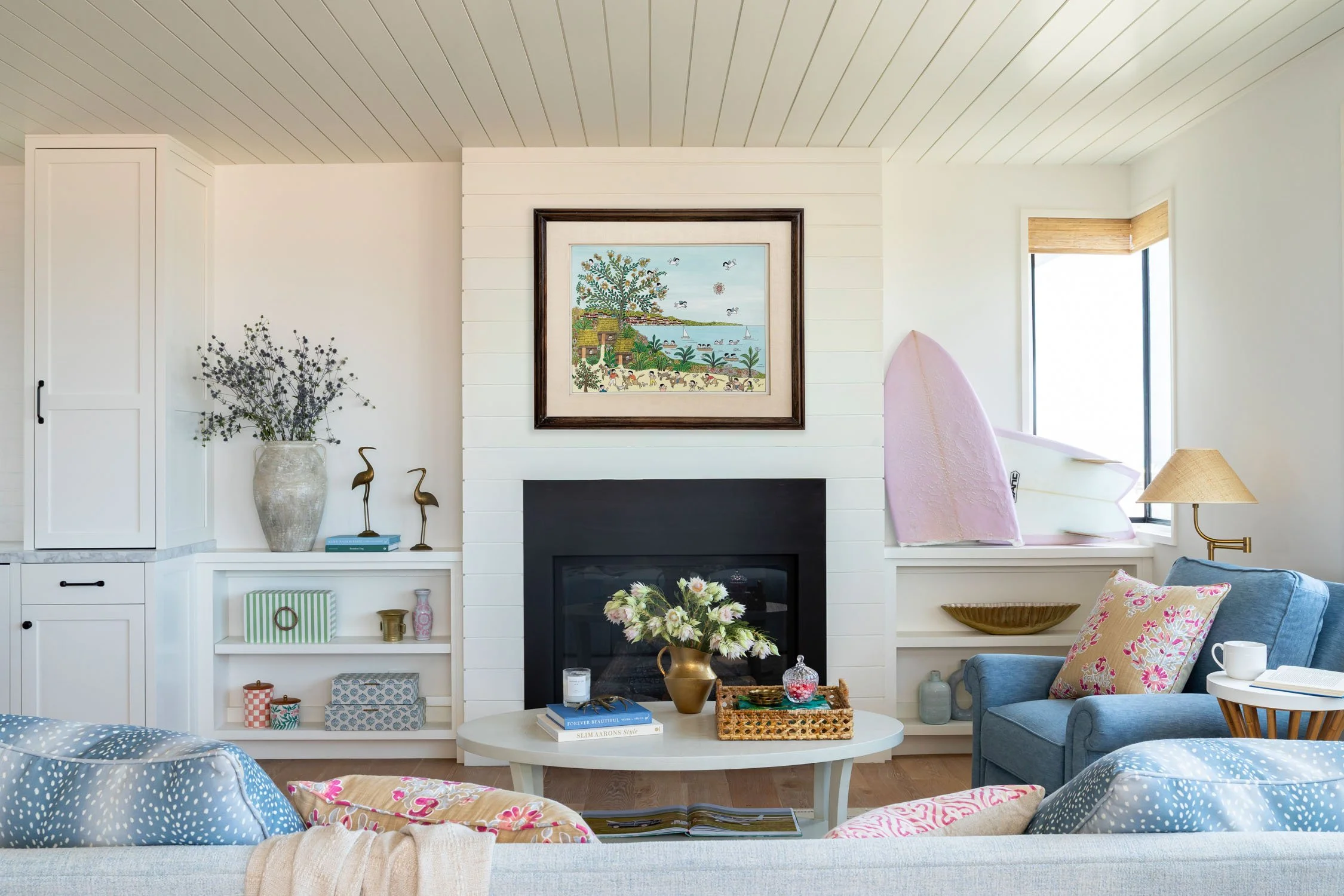 Coastal living room with fireplace, built-in shelving, blue seating, and colorful accents in Manhattan Beach by JKB Home Design
