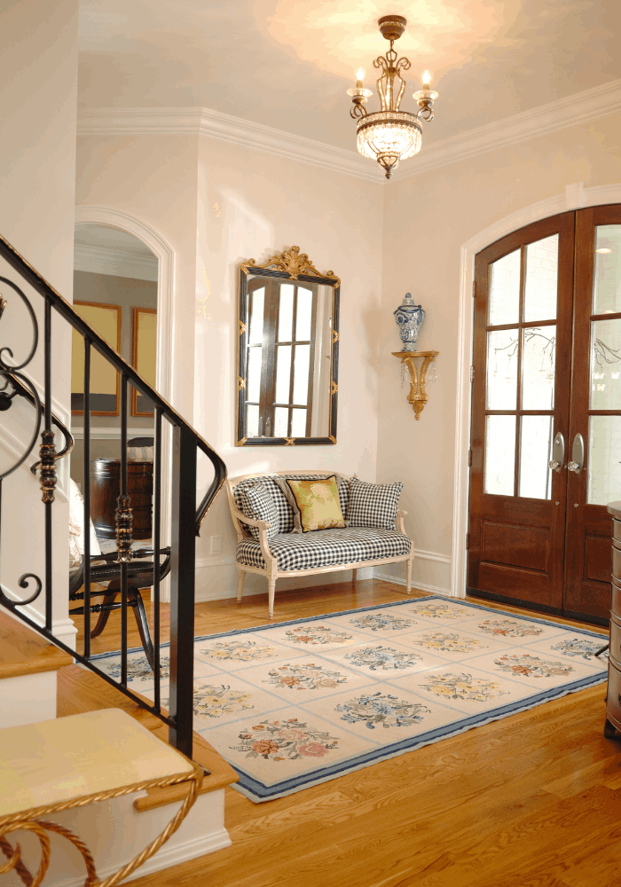 Traditional foyer with patterned area rug, upholstered bench, decorative mirror, chandelier, and wood front door