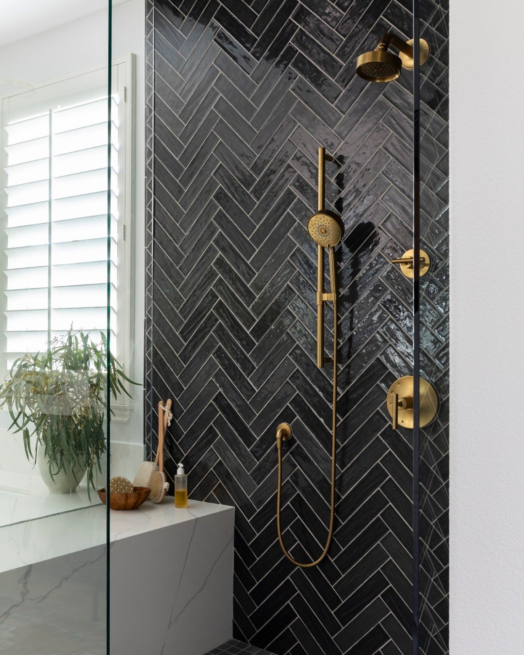 Let&rsquo;s take a moment to appreciate how the Crimson Canyon shower came together. We chose a rich, moody herringbone tile and combined it with the warmth of @kohler x @studiomcgee brass hardware. This combination creates a space that feels both ti