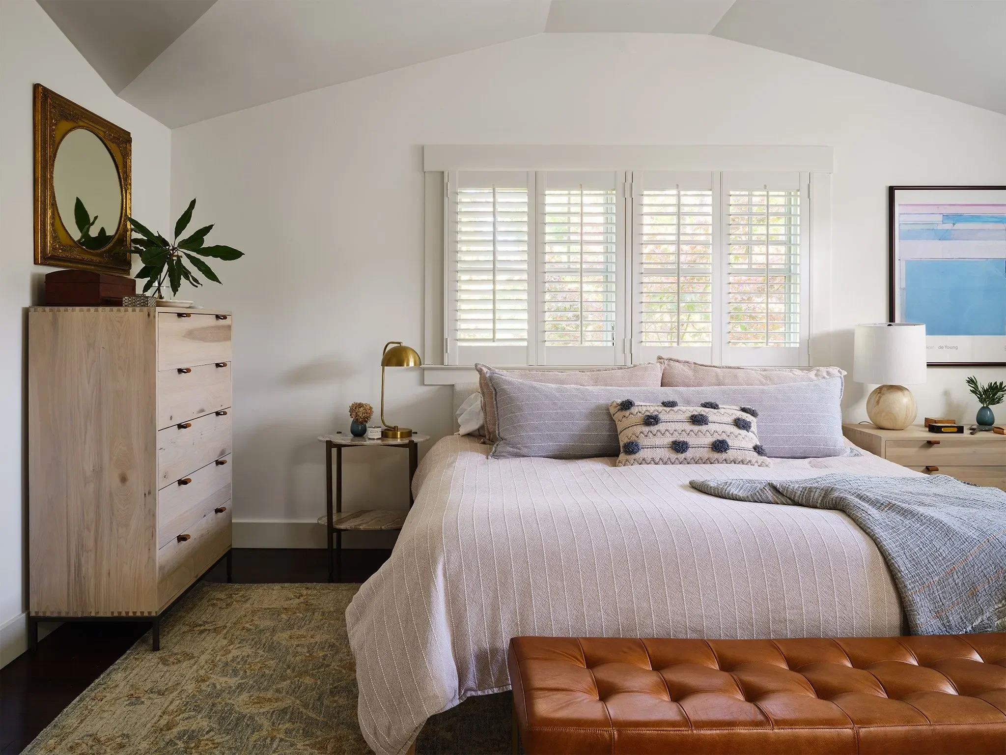 Serene San Anselmo bedroom with pale wood dressers, neutral bedding, leather bench, and layered artwork by Julie Beuerlein