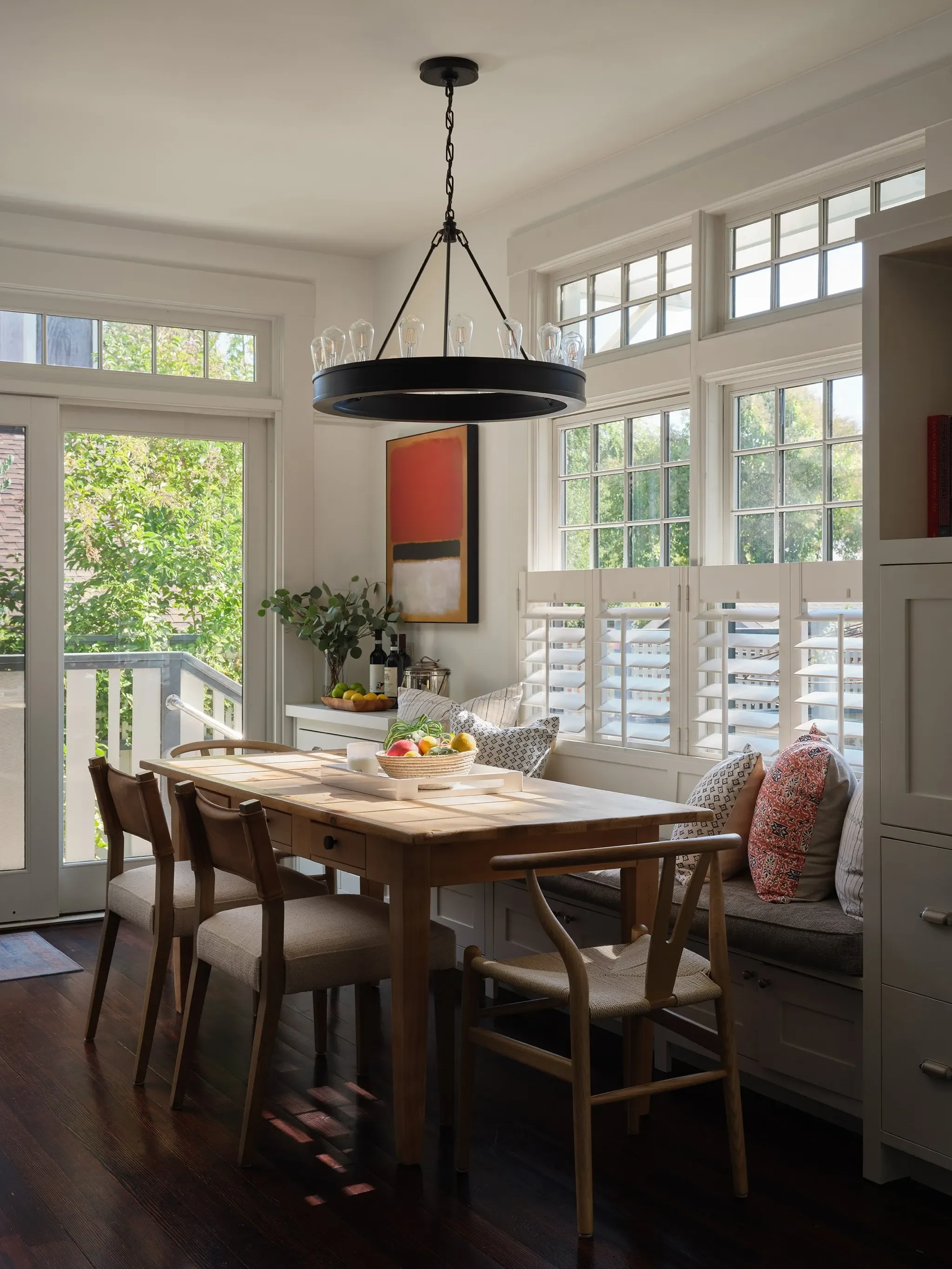 Bright San Anselmo dining nook with wood table, built-in bench seating, colorful pillows, and garden views