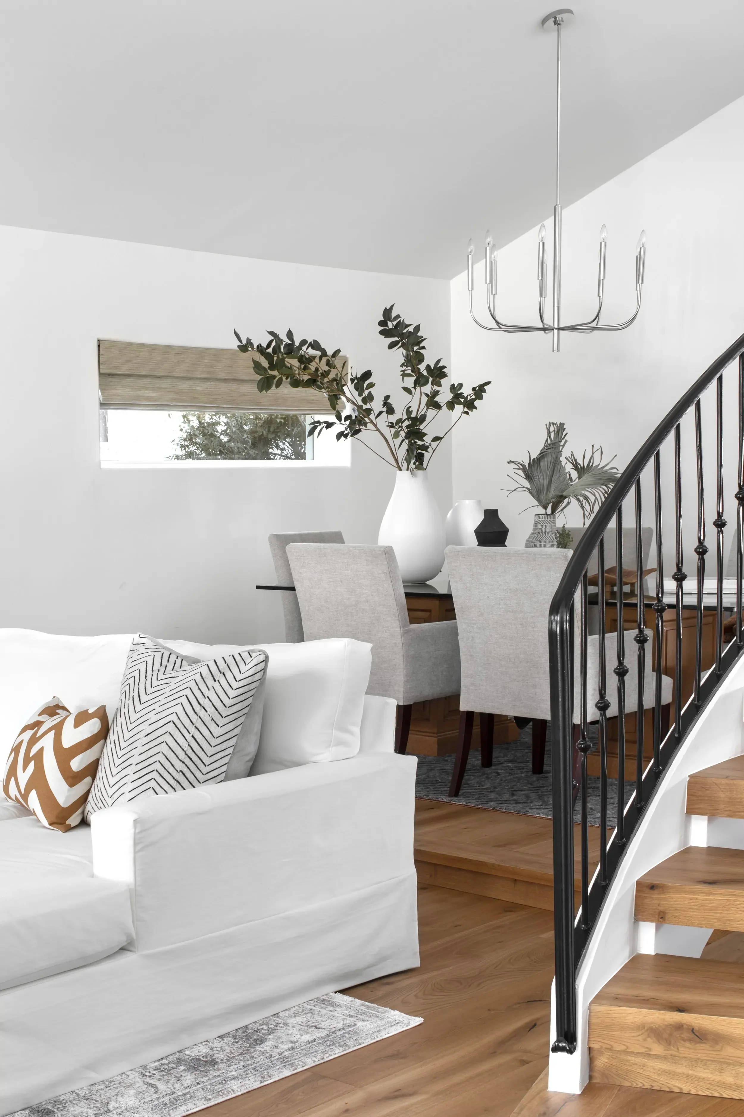 Open living and dining space with oak staircase, white seating, and modern chandelier in Pacific Palisades, designed by Julie Beuerlein