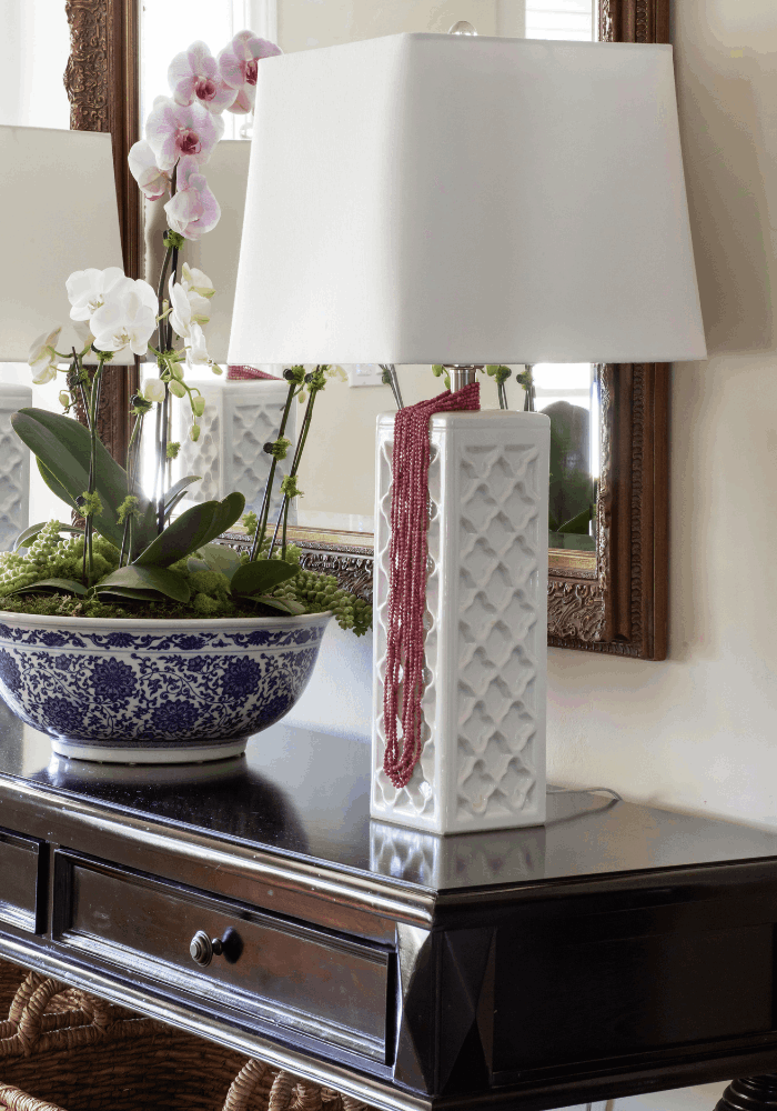 Entry console styled with blue and white orchid planter, white table lamp, and decorative mirror