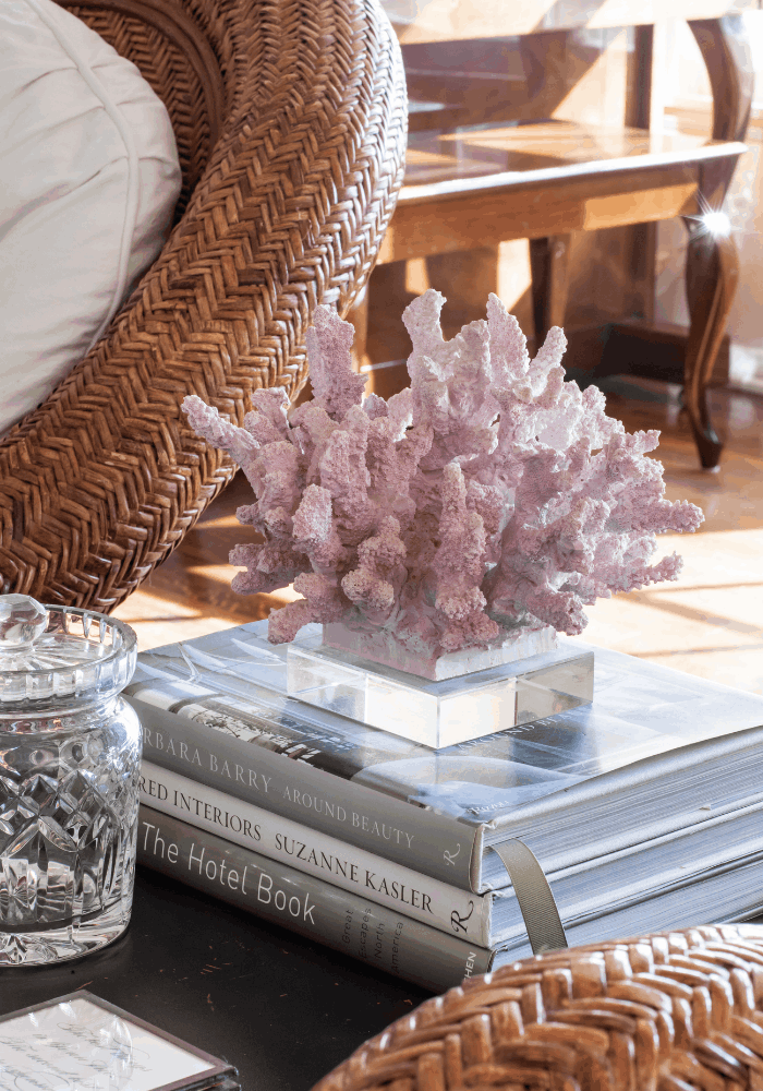 Pink coral displayed on stacked interior design books beside a woven chair and glass accessory in Palos Verdes, CA home