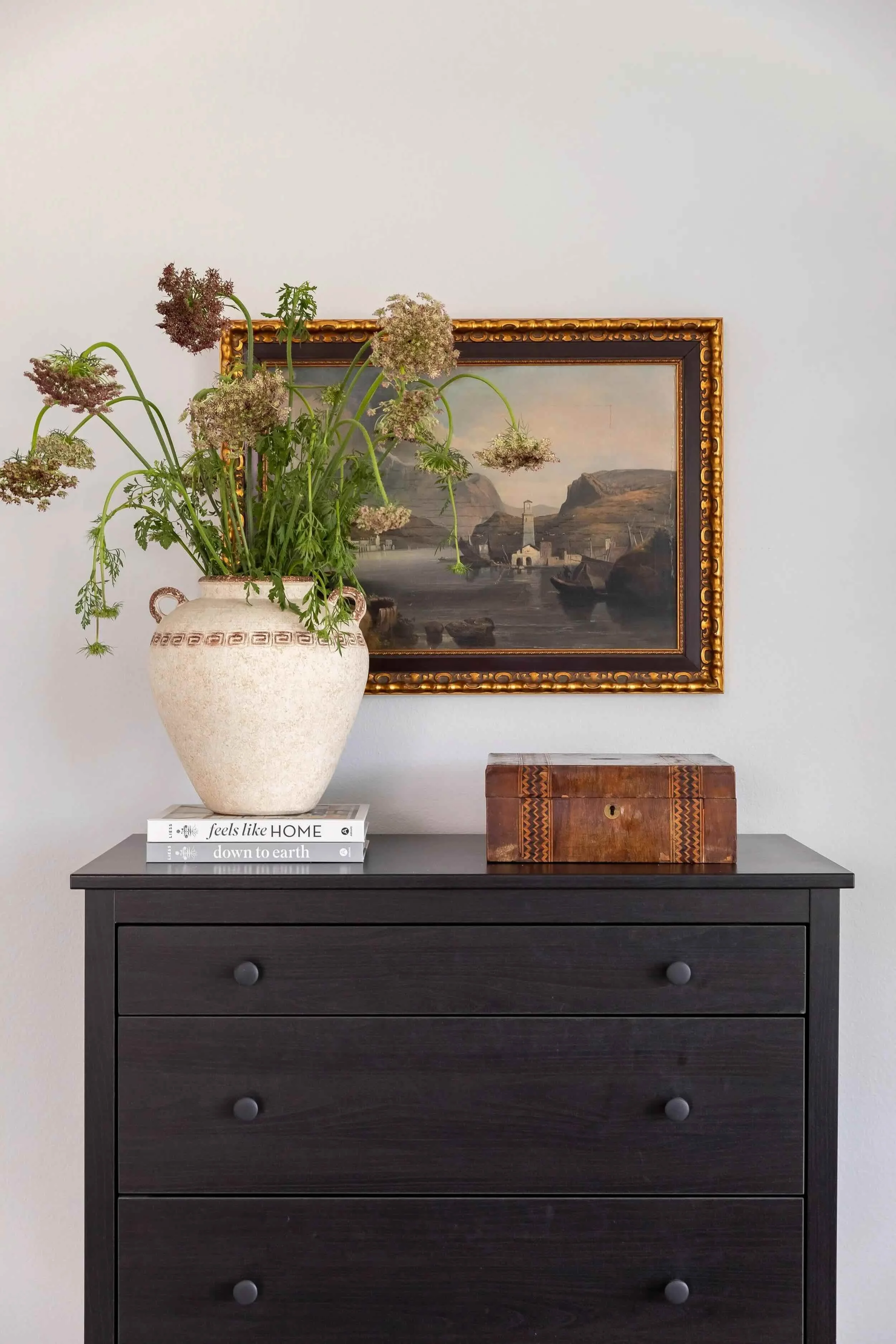 Dark wood dresser styled with vintage artwork, books, and organic florals, designed by JKB Home Design