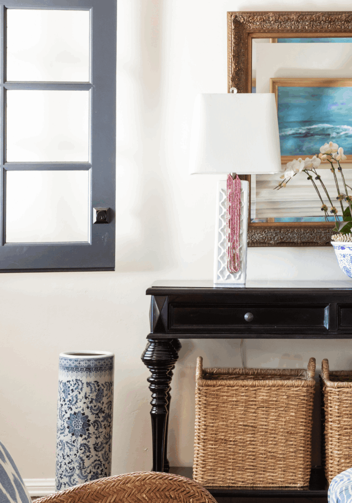 Dark wood foyer console with table lamp, blue and white accessories, mirror, and woven storage baskets
