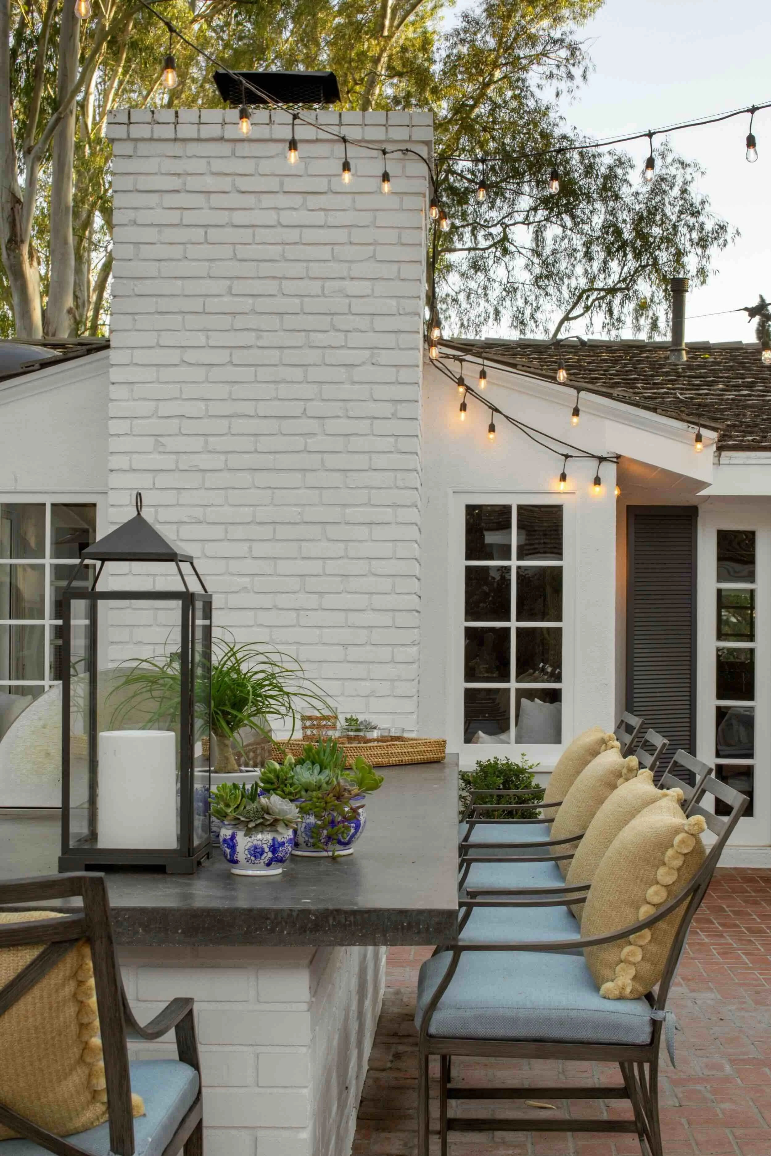 Outdoor kitchen and bar with string lights, cushioned seating, and layered accessories, designed by JKB Home Design in Southern California
