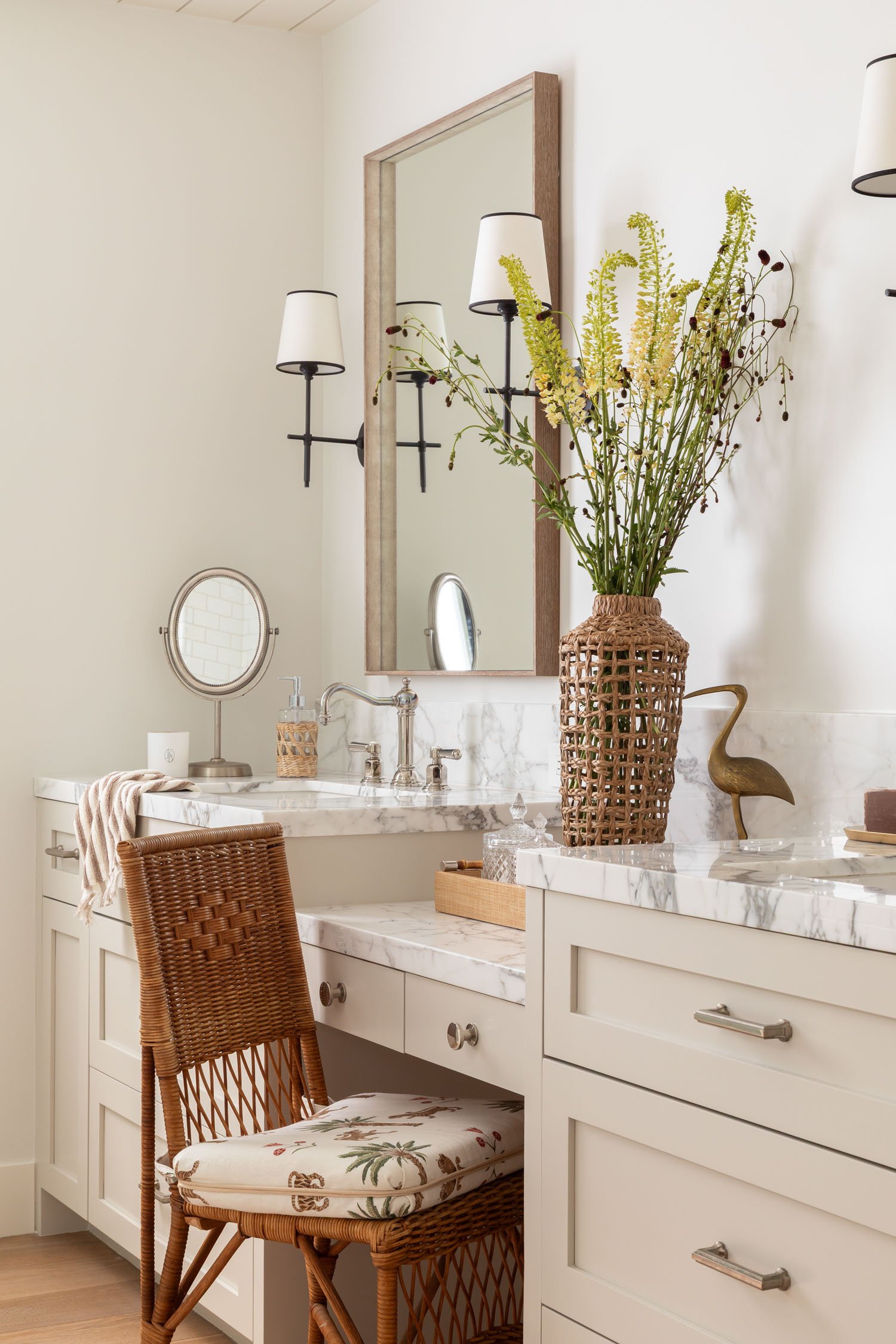 Refined bathroom vanity with marble countertops, woven chair, and wall sconces in Manhattan Beach, designed by Julie Beuerlein