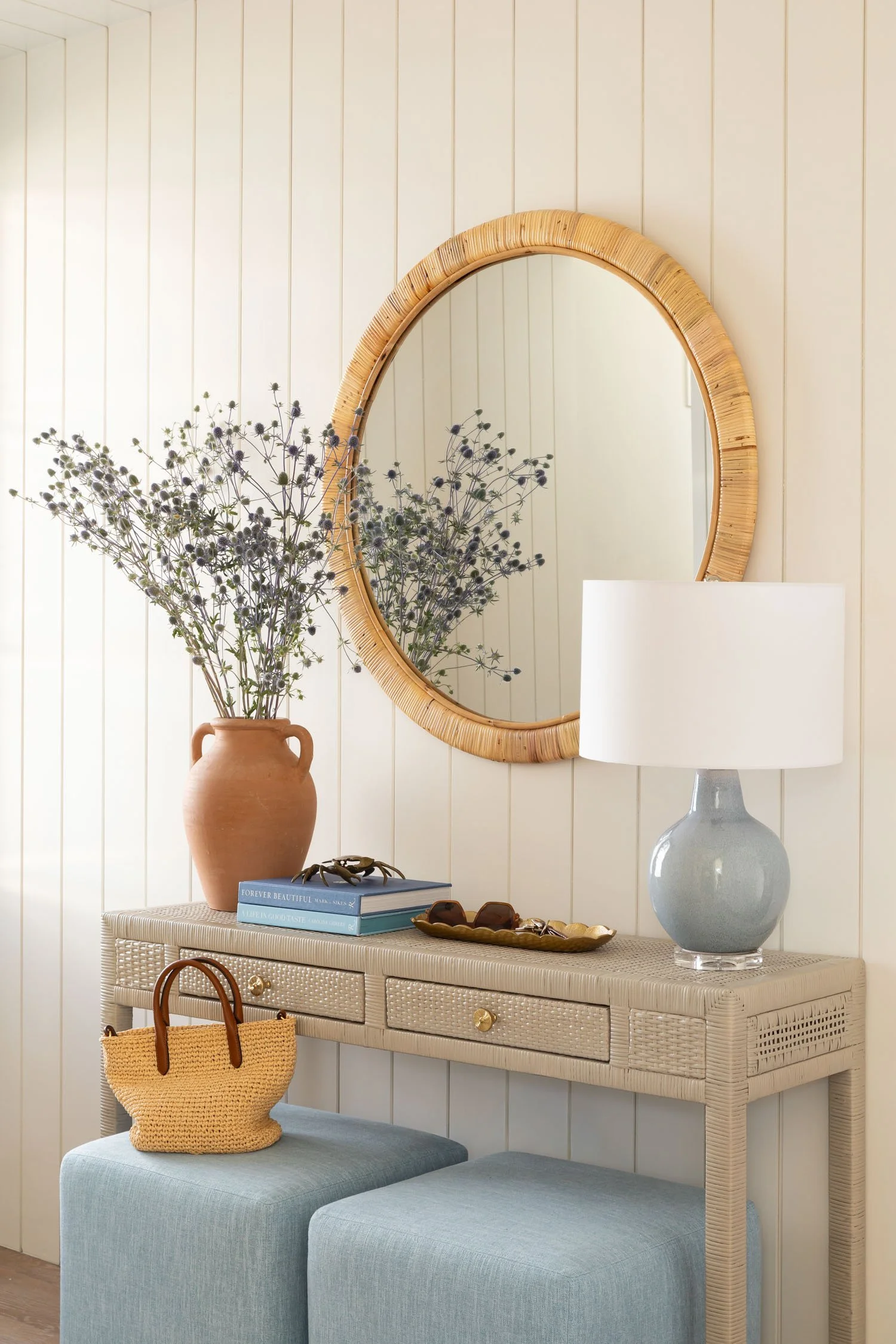 Woven console table with rattan mirror, blue stools, and layered decor in a Manhattan Beach home by JKB Home Design