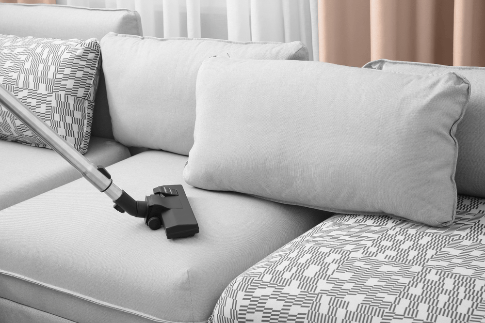 Light gray sofa being vacuumed as part of a spring deep-cleaning routine