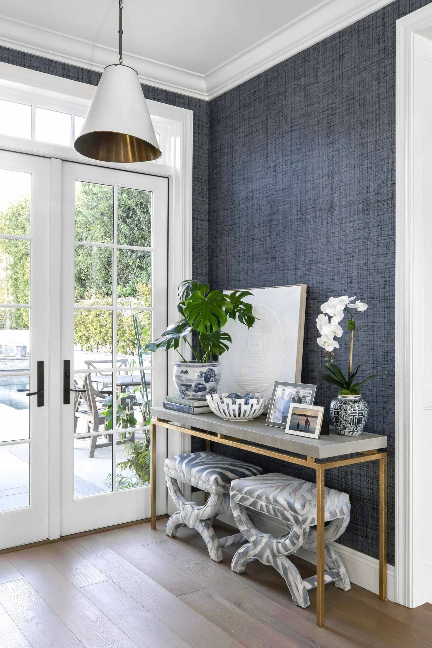 Stone entry table with orchids and books against blue wallpaper, designed by JKB Home Design, Pacific Palisades