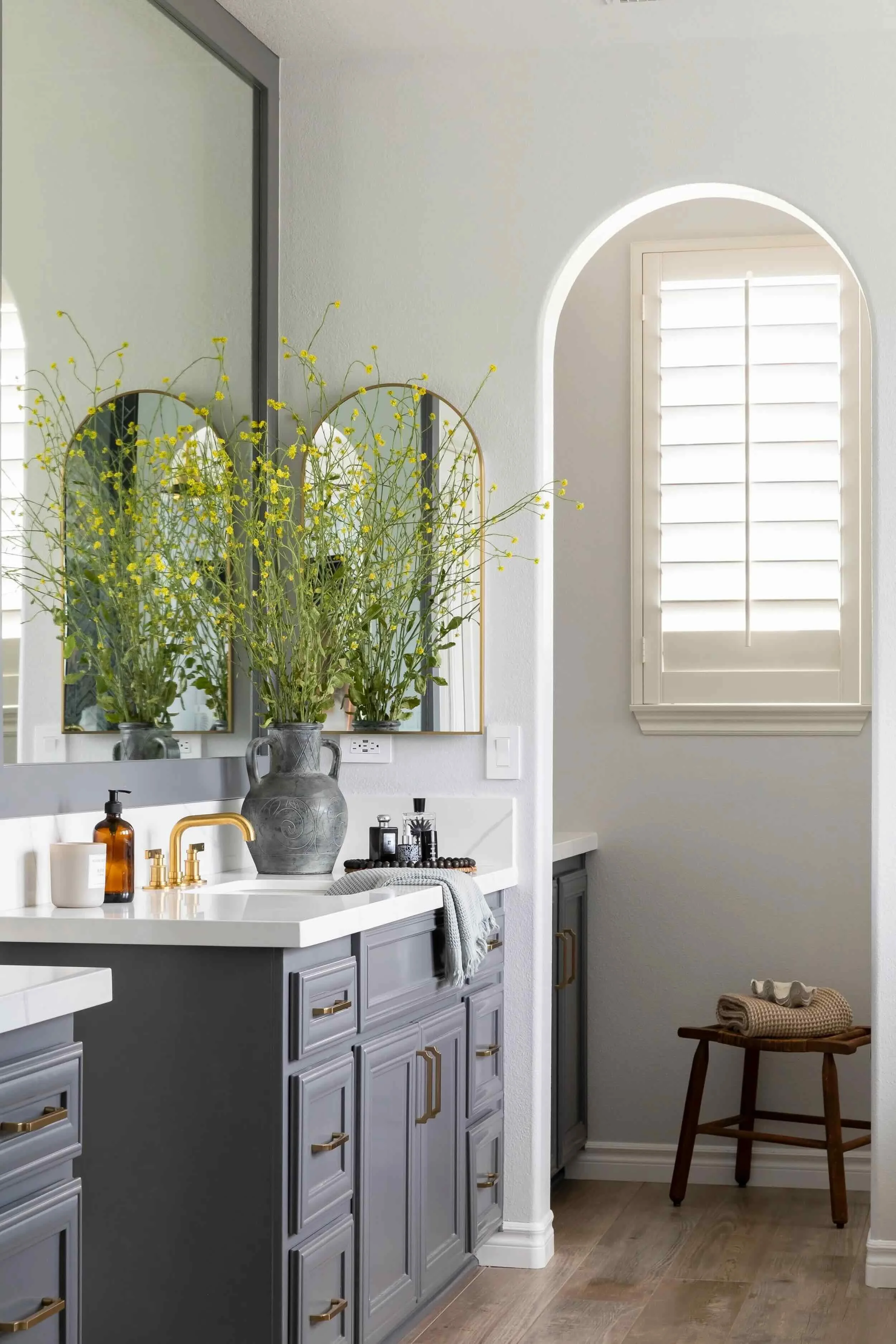 Bathroom with gray cabinetry, brass hardware, arched doorway, and layered styling, designed by JKB Home Design