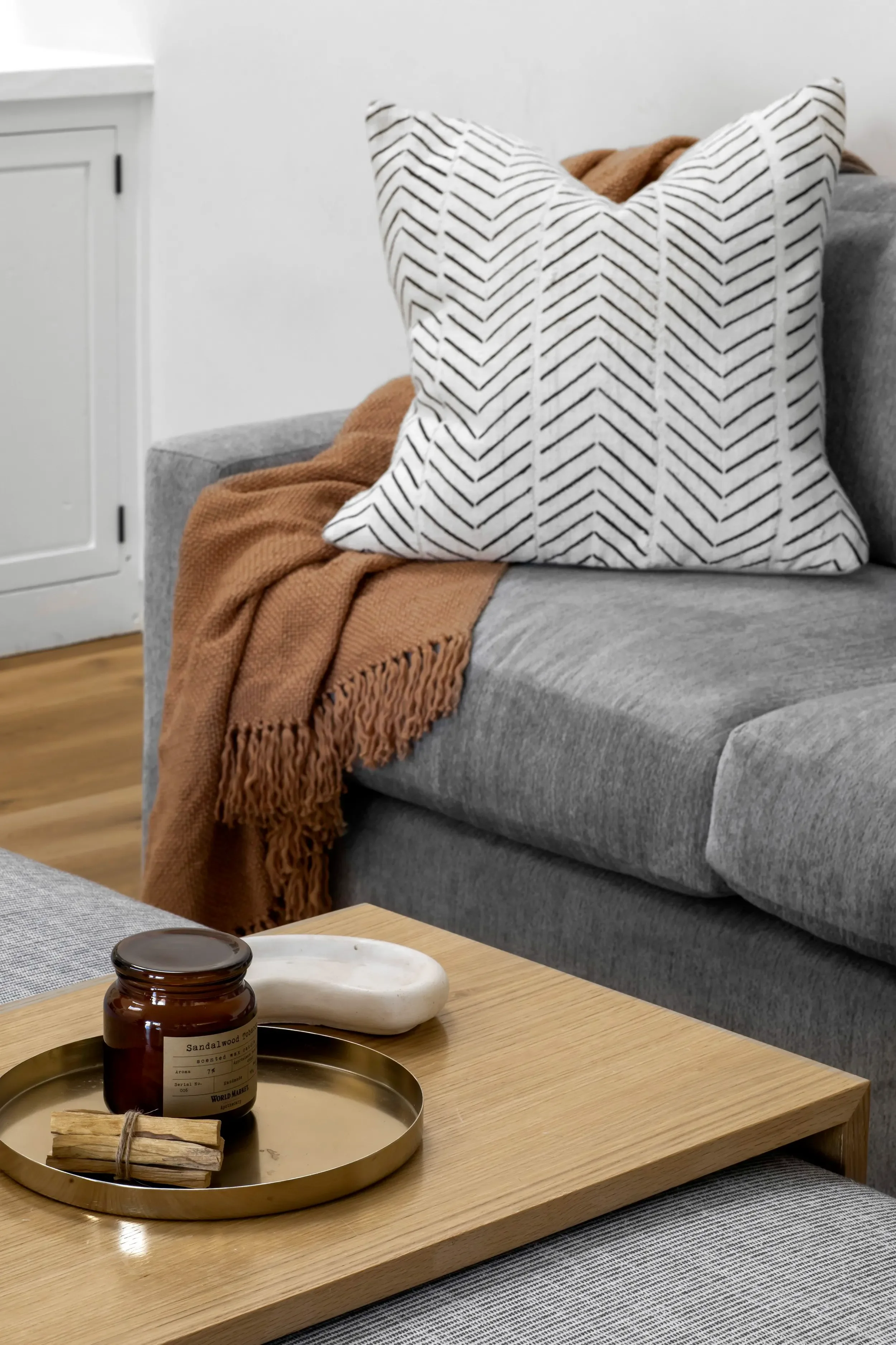 Cozy Pacific Palisades living room detail with gray sofa, patterned pillow, warm throw, candle, and wood coffee table designed by Julie K. Beuerlein