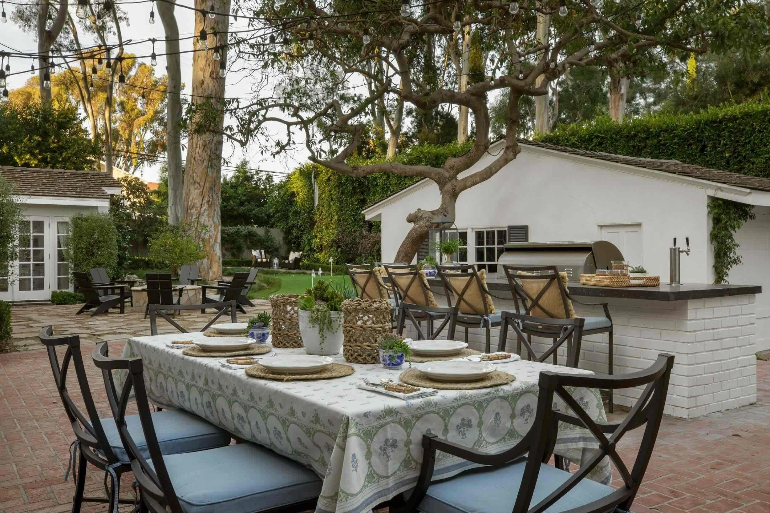Outdoor dining area with set table, string lights, fire pit, and built-in bar, designed by JKB Home Design in Southern California