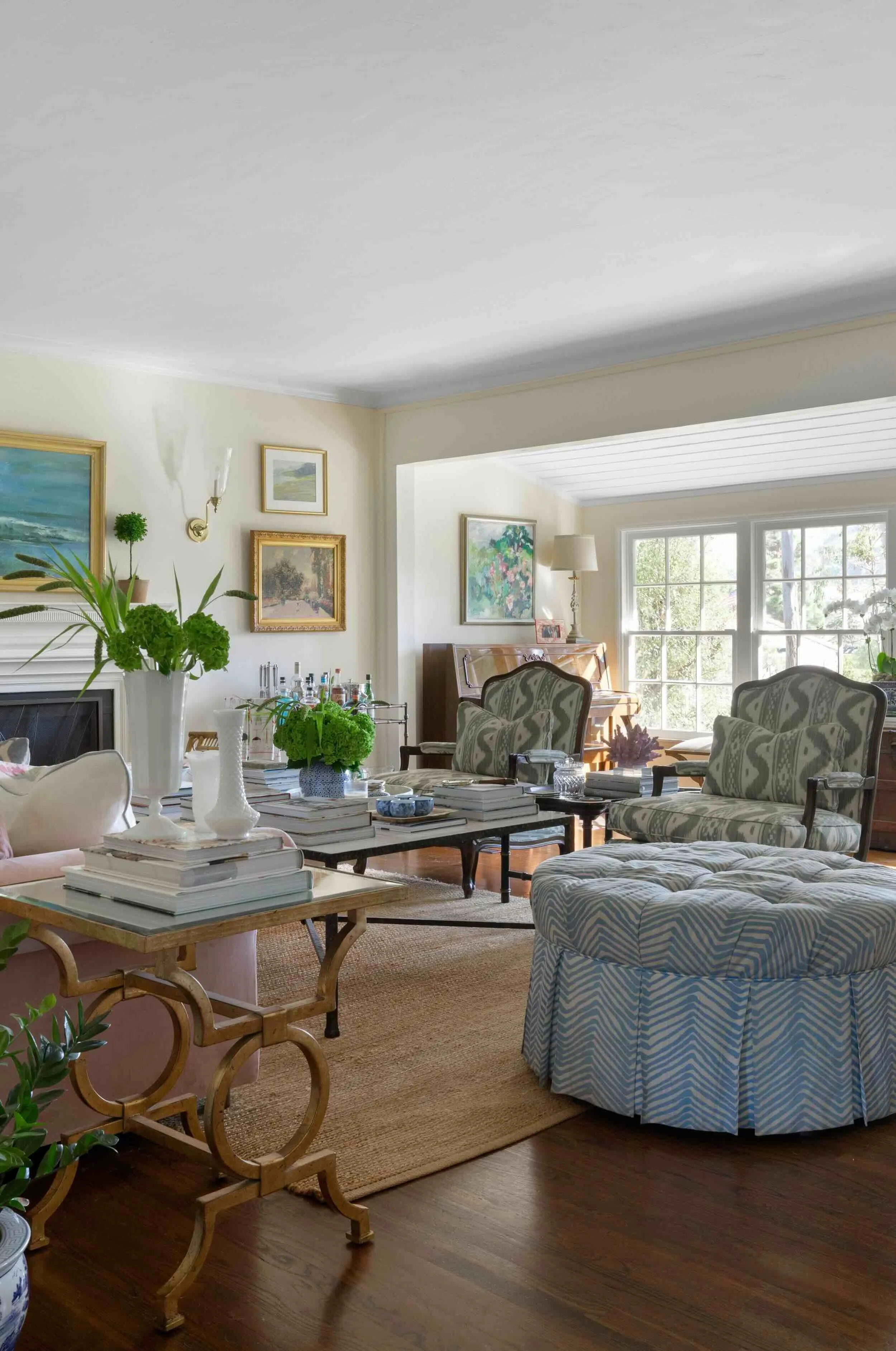 Eclectic living room with upholstered ottoman, vintage-style chairs, natural fiber rug, and layered furnishings by JKB Home Design