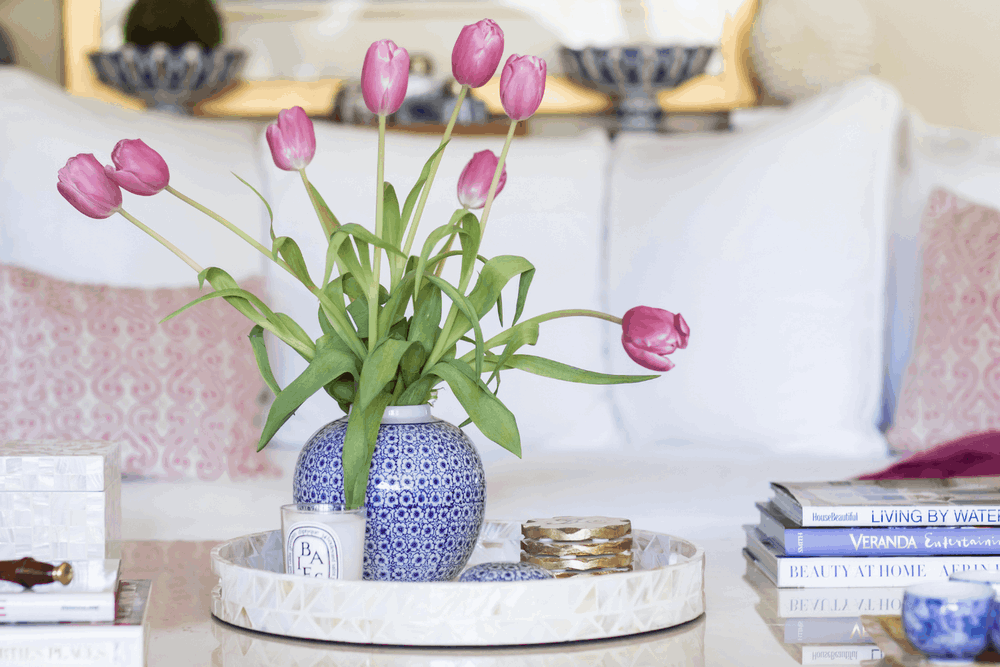 Coffee table styled with pink tulips, blue and white ceramic vase, decorative tray, candle, and stacked design books arranged by JKB Home Design