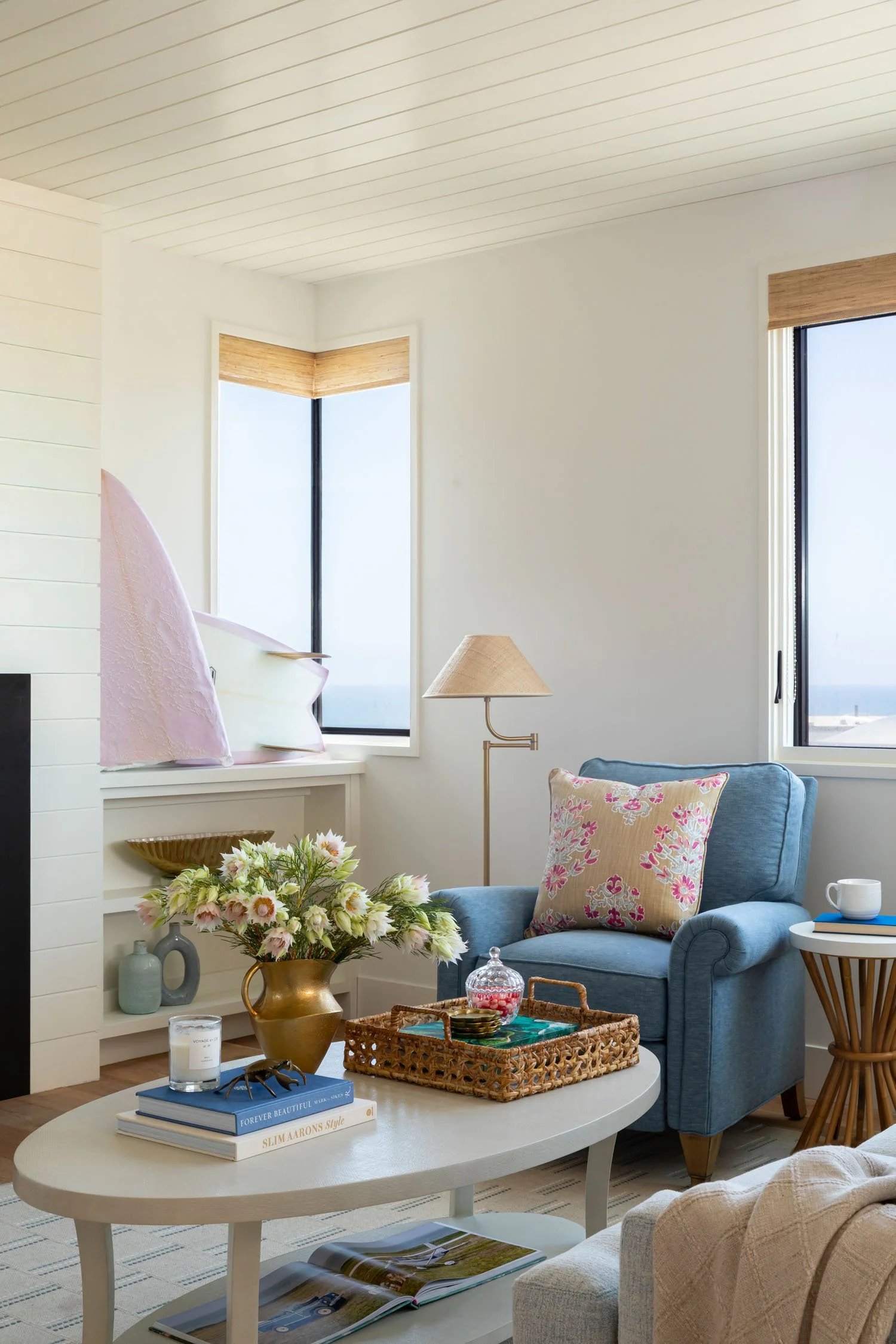 Bright Manhattan Beach living room with white fireplace, built-in shelving, blue armchairs, and layered coastal decor by JKB Home Design