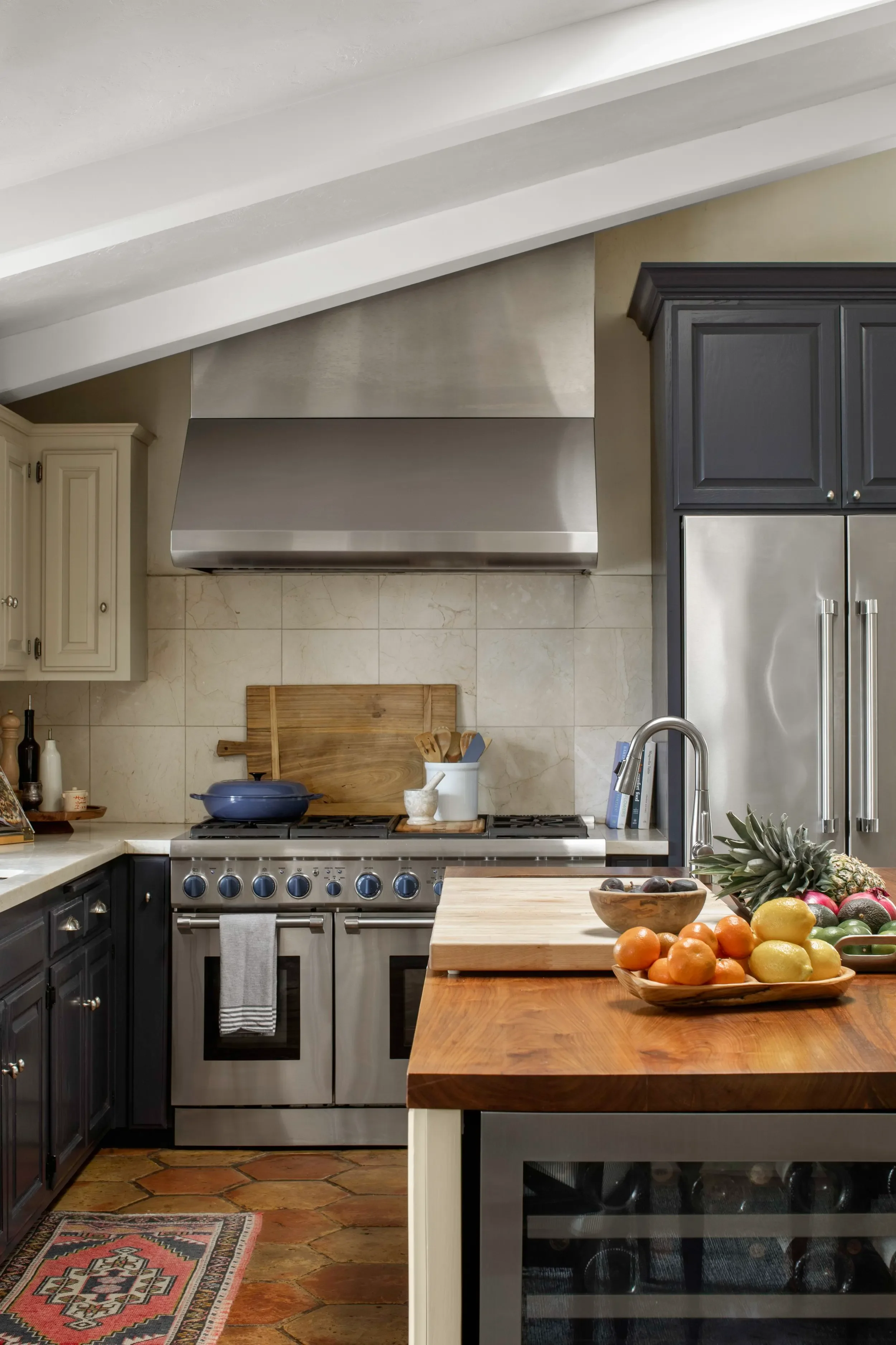 Warm kitchen with professional range, wood island, dark cabinetry, and terracotta flooring, designed by JKB Home Design