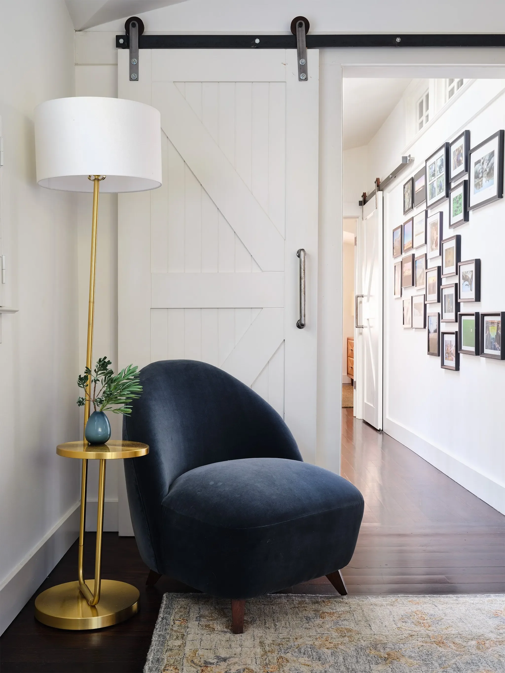 San Anselmo sitting area with blue velvet chair, brass table, white barn door, and gallery wall, designed by Julie Beuerlein