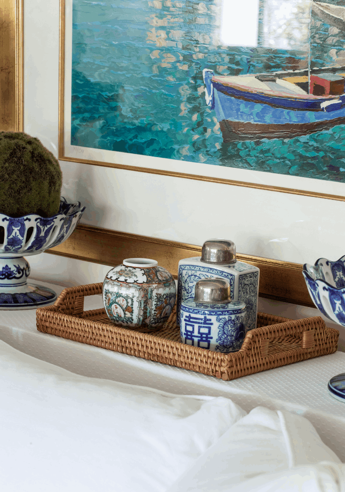 Woven tray styled with blue and white porcelain jars beneath colorful coastal artwork, interior designed by Julie K Beuerlein