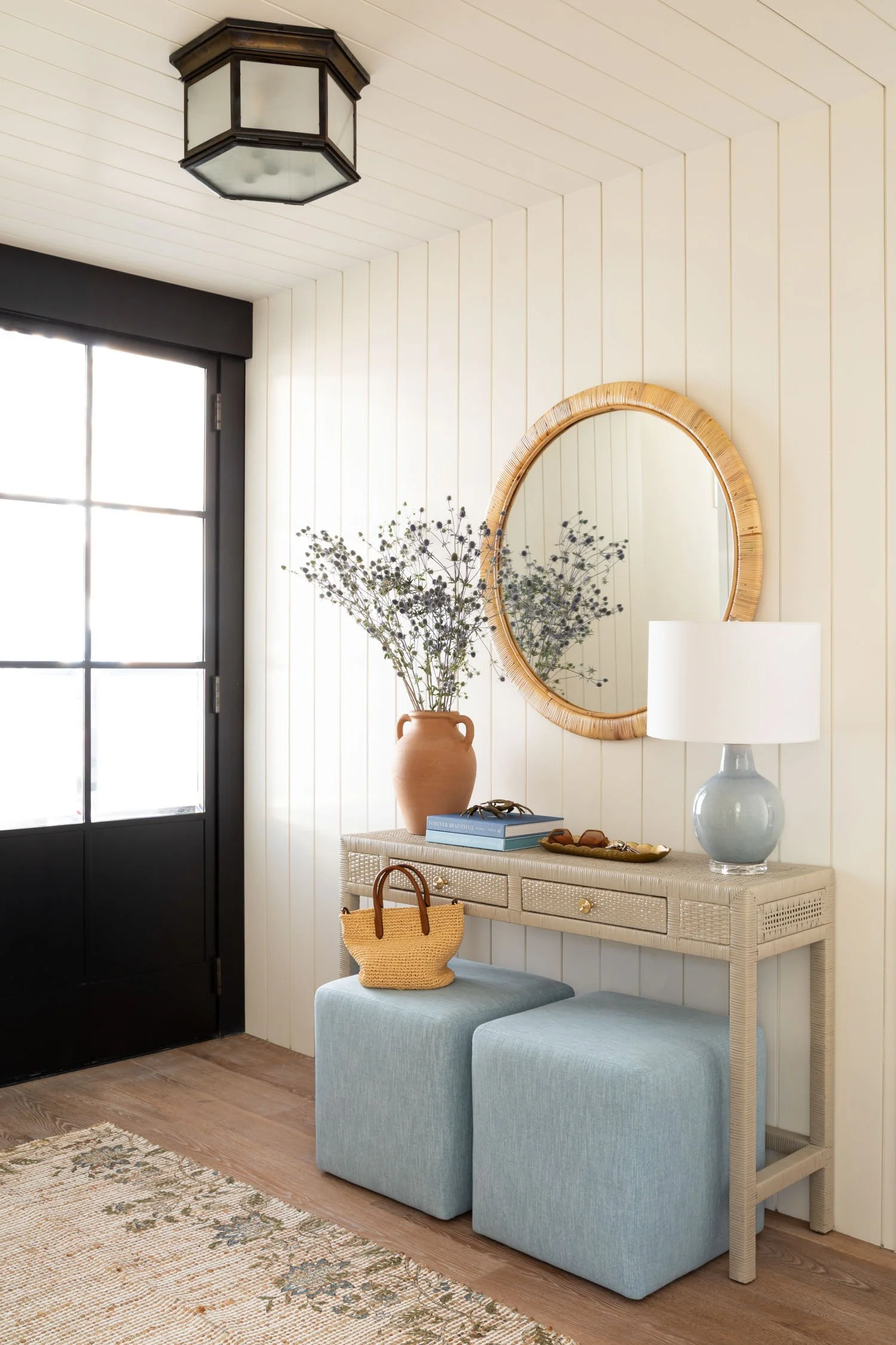Bright Manhattan Beach entryway with woven console, round rattan mirror, and blue upholstered stools, designed by Julie Beuerlein