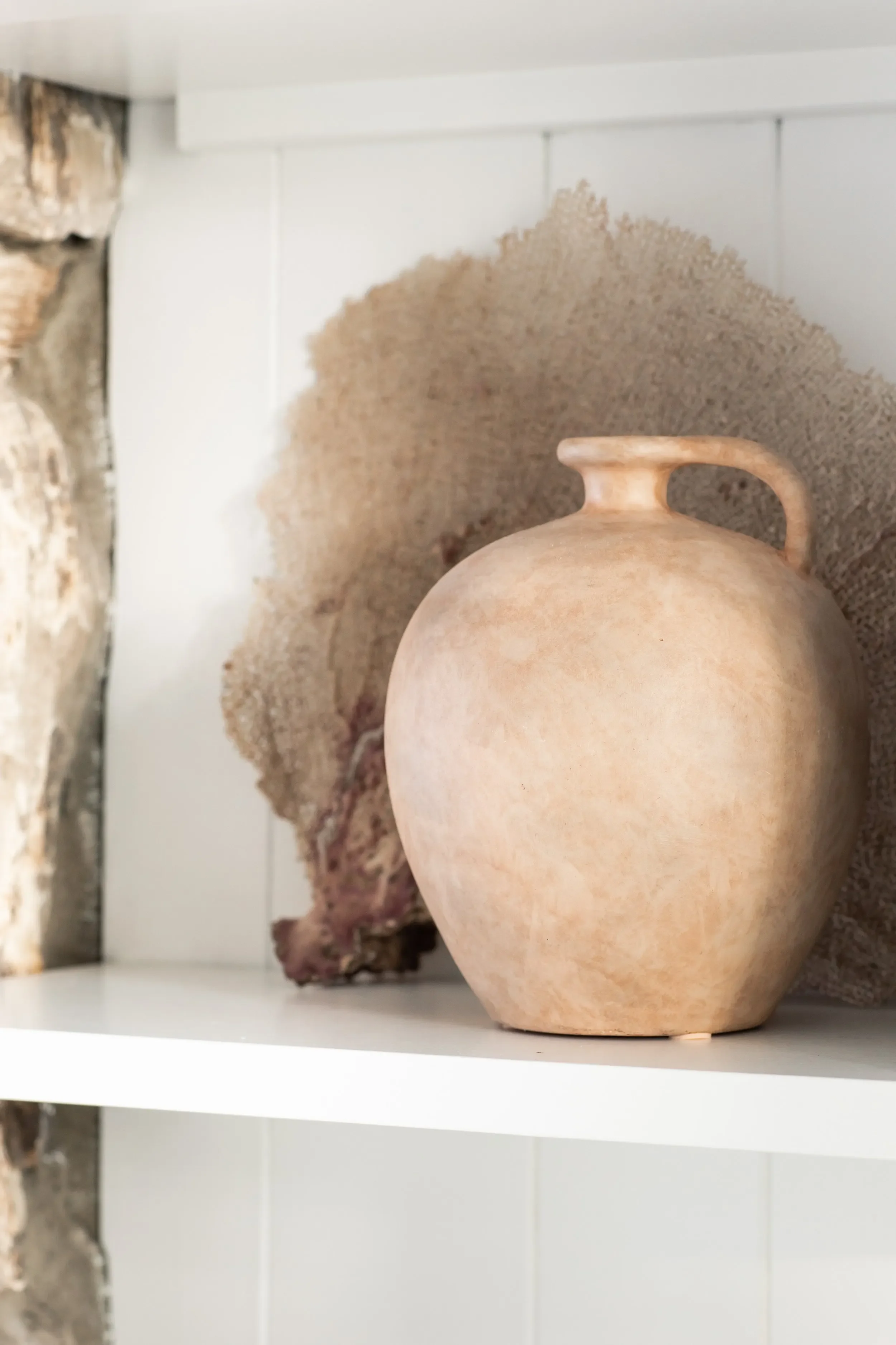 Styled built-in shelf with sculptural pottery and natural textures beside a stone fireplace in Palos Verdes Estates by JKB Home Design