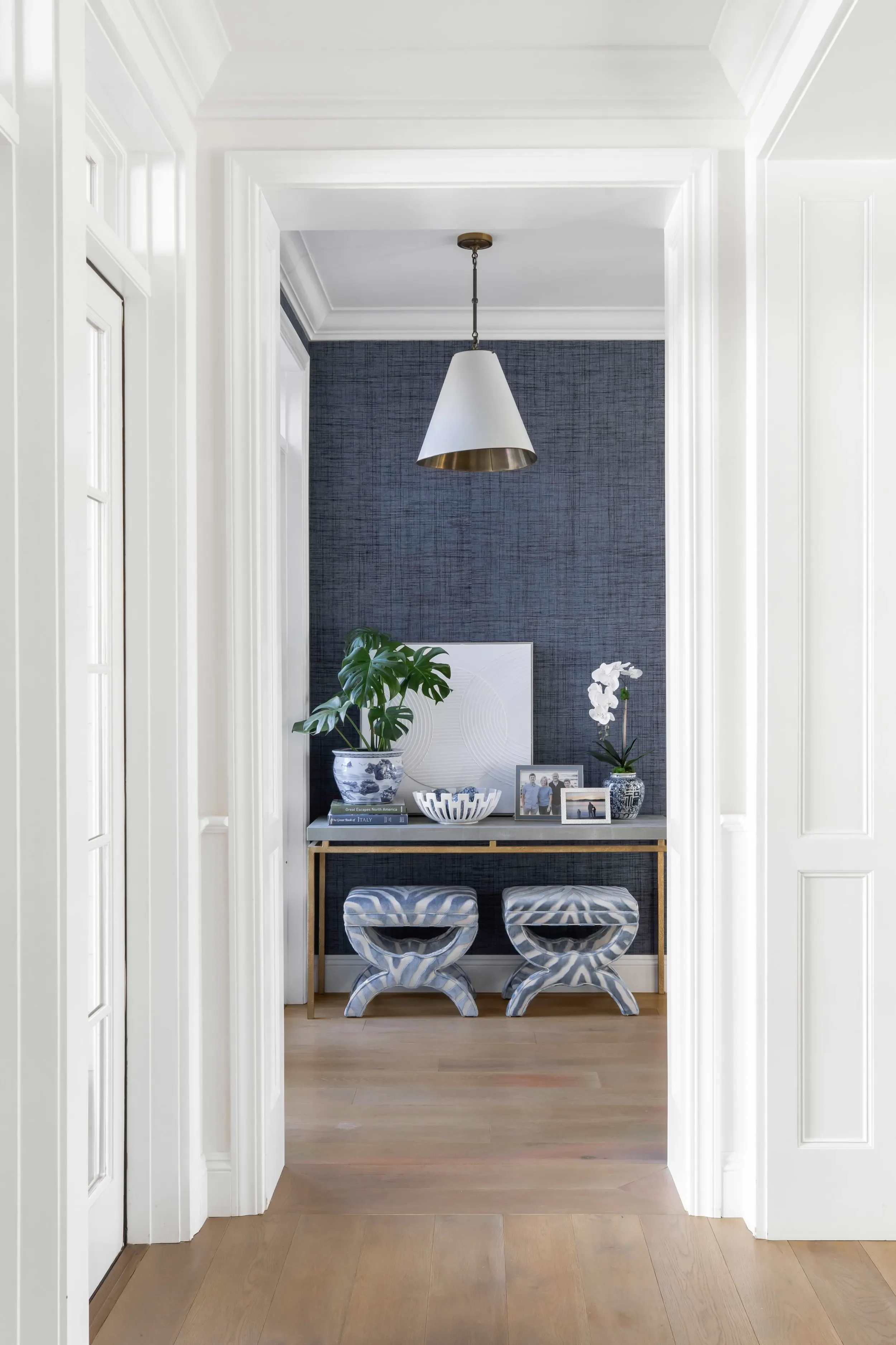 Traditional entry with blue textured walls, brass console, patterned stools, and white millwork in Pacific Palisades by JKB Home Design