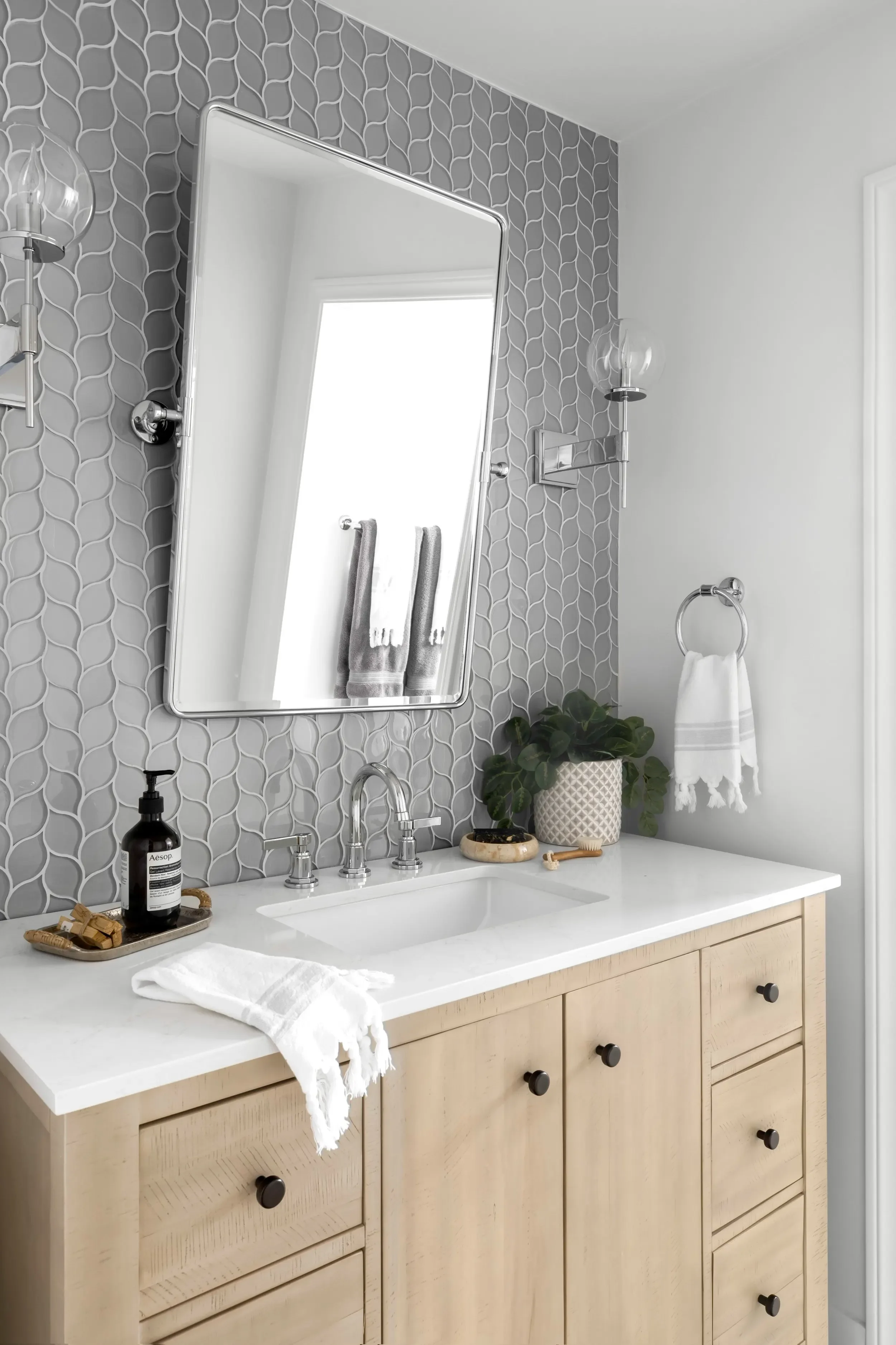 Powder room with natural wood vanity, gray patterned tile wall, and polished chrome fixtures in Pacific Palisades by JKB Home Design