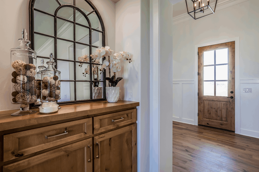 Entryway console with oversized arched mirror, orchids, decorative accessories, and wood front door