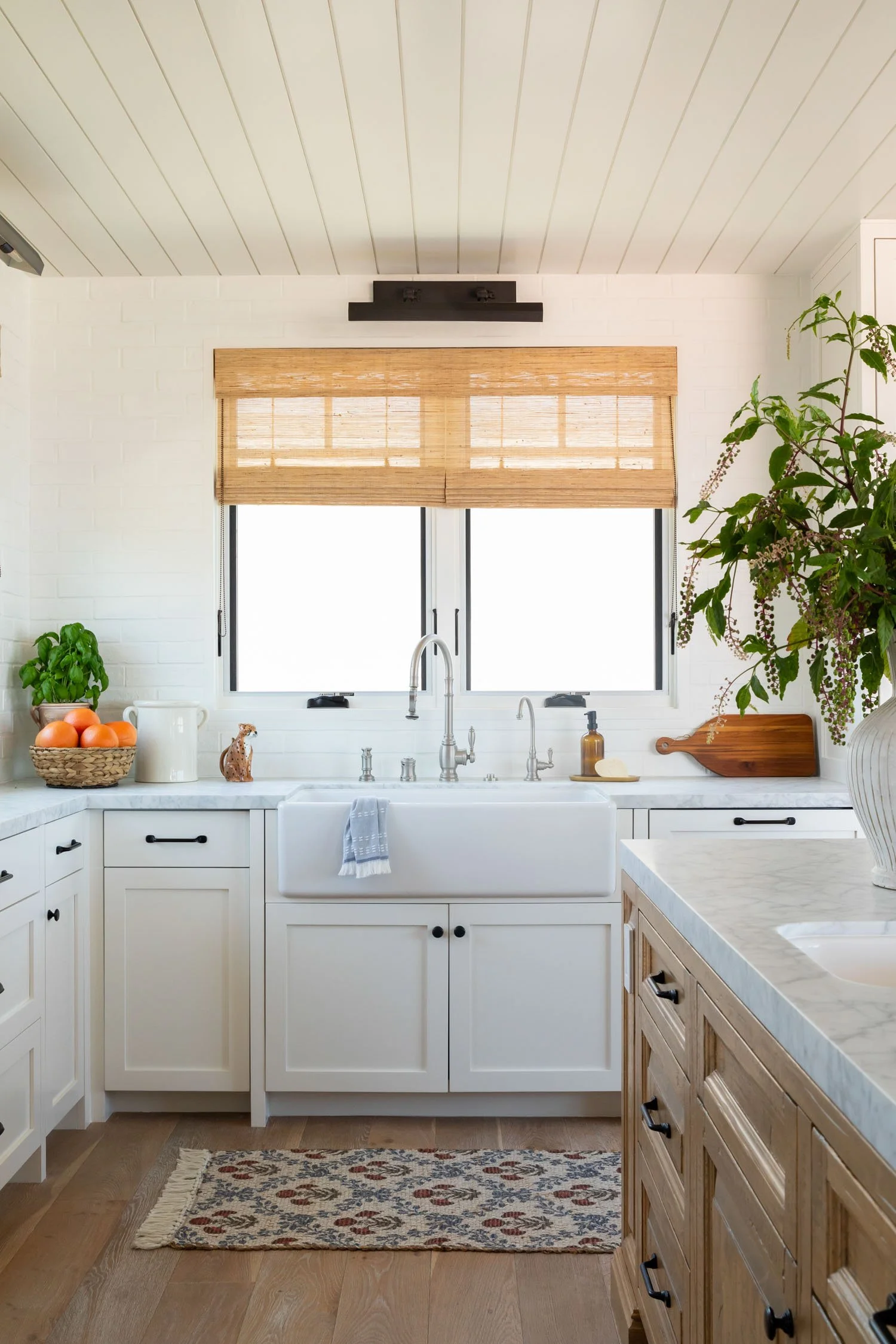 Bright Manhattan Beach kitchen with white cabinetry, natural wood island, marble countertops, and black pendant lights, designed by Julie Beuerlein