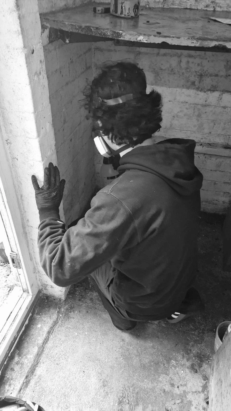 A man cleaning black mold from a ceiling with a cloth, wearing a Dampsafe branded T-shirt in a home interior.