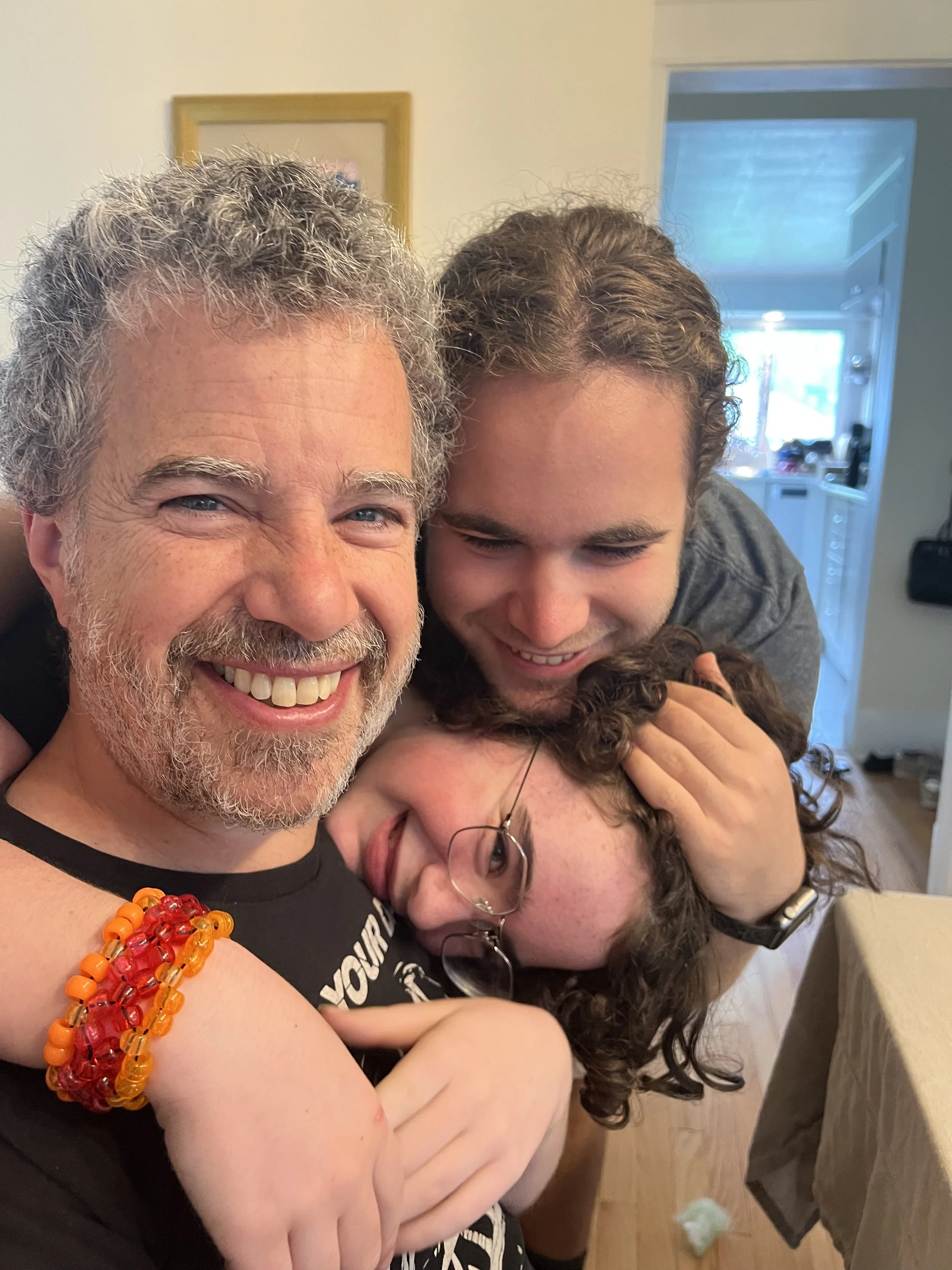 Rabbi Jonathan Freirich smiling and being hugged by his son and daughter inside a home, with a kitchen background visible.