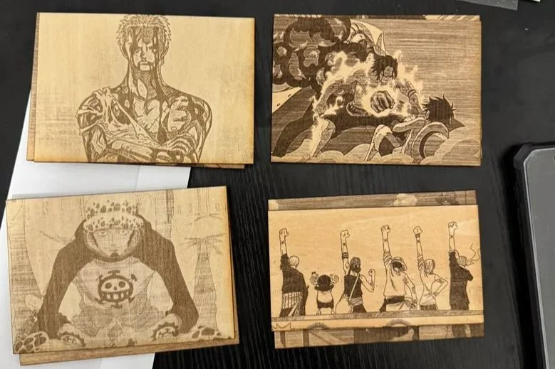 Four wooden plaques with engraved cartoon-style artwork of characters from popular anime and manga series, placed on a black surface.