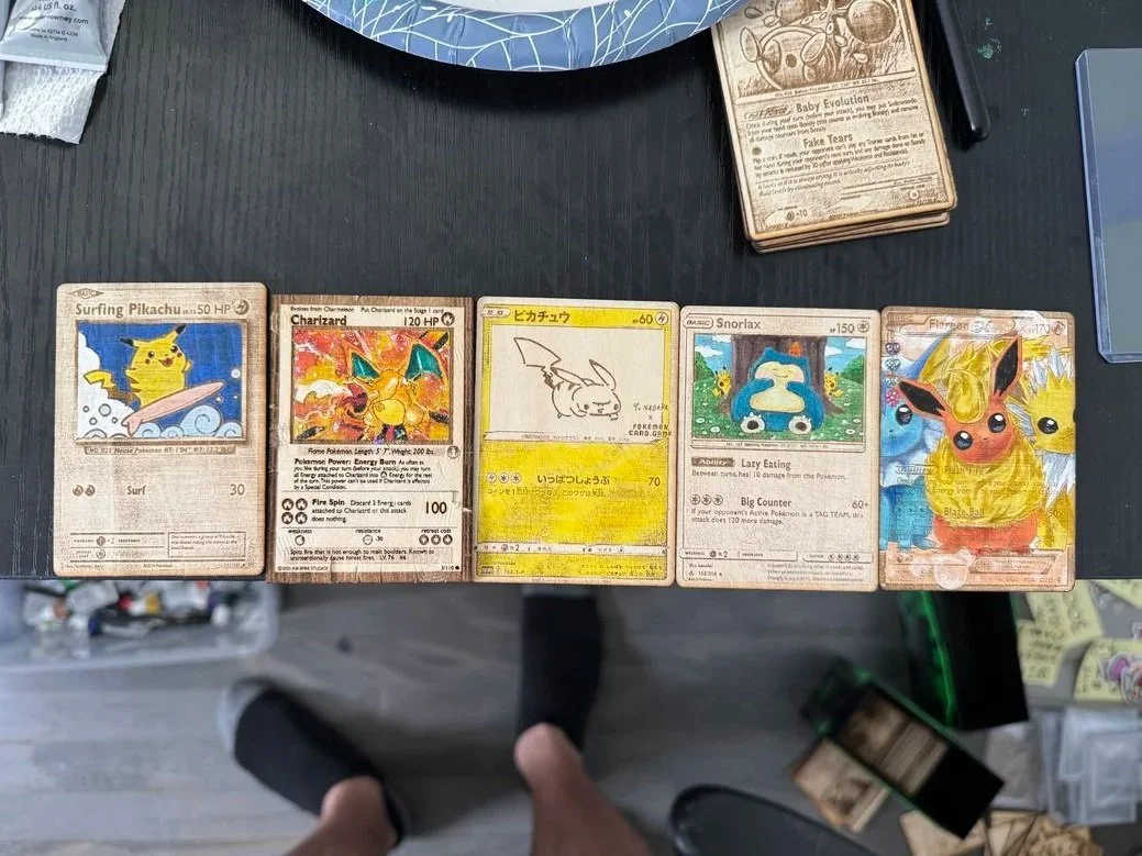 Five vintage Pokémon trading cards laid out on a black surface, featuring Surfing Pikachu, Charizard, a yellow Pikachu sketch, Snorlax, and Flareon.