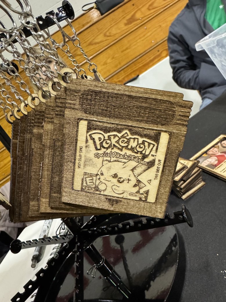 Wooden keychains featuring Pikachu from Pokémon, with engraved artwork and text, hanging on a display rack.
