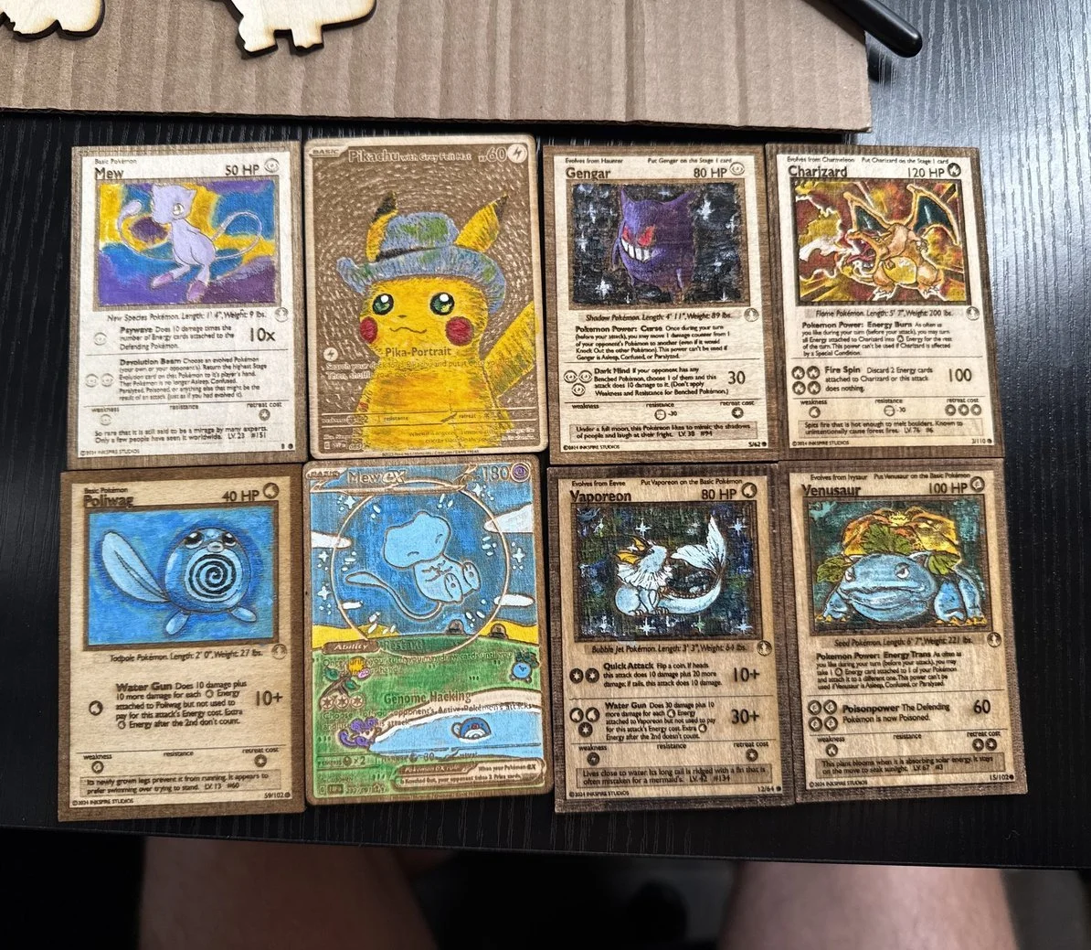 Collection of eight Pokémon cards on a wooden surface. The cards include Mew, Pikachu, Gengar, Charizard, Poliwag, Mewex, Vaporeon, and Venusaur.