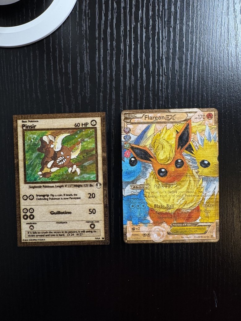 Two Pokémon cards, Pinsir and Flareon EX, lying on a black wooden surface.