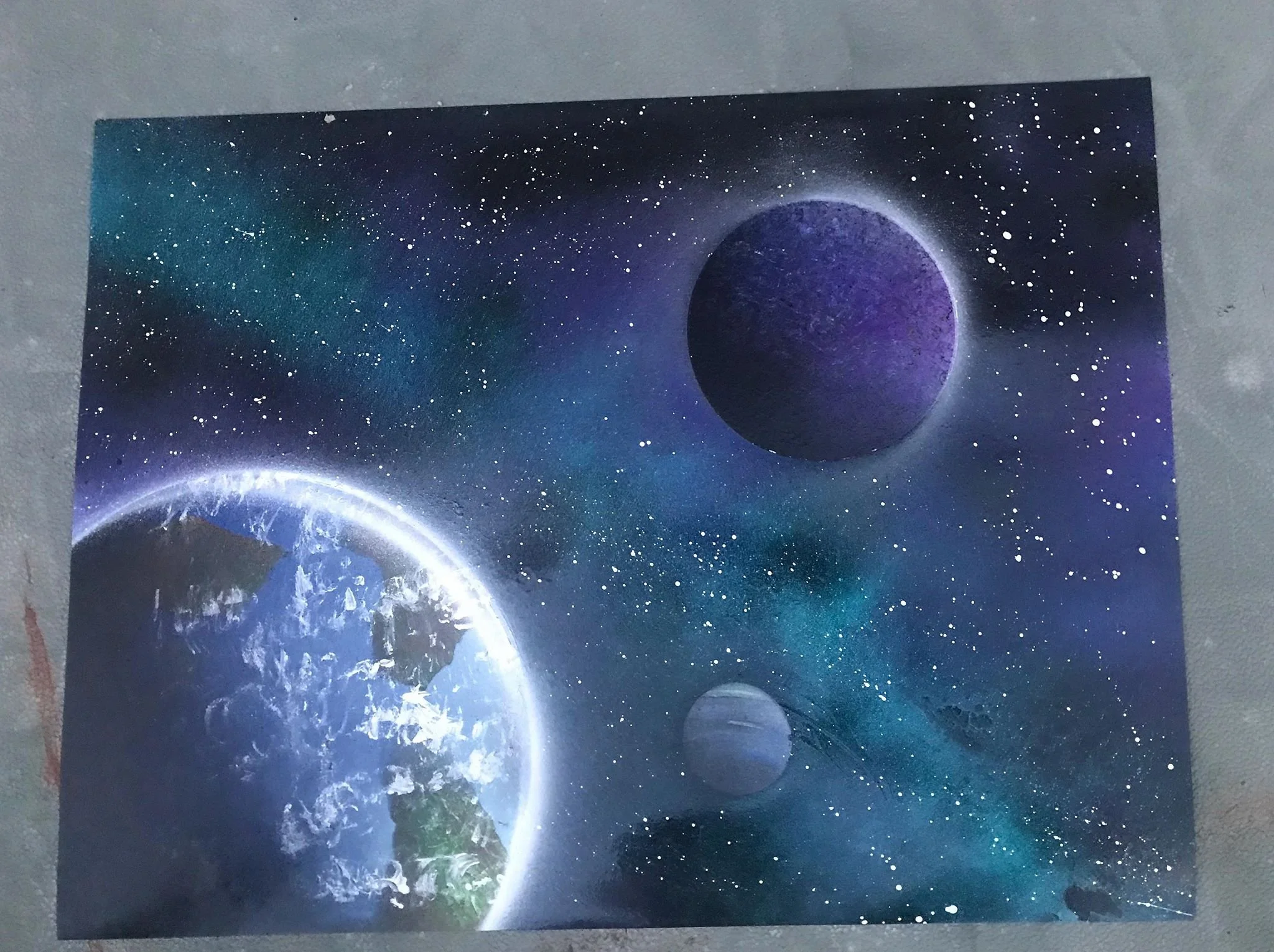 Airbrushed painting of space featuring Earth, two moons or planets, and a star-filled galaxy background.