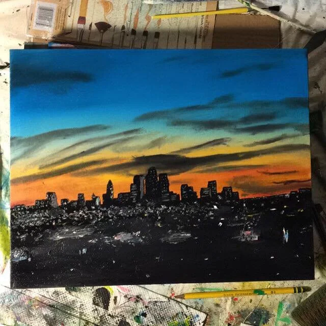A painting of a city skyline at sunset with a colorful sky of blue, yellow, orange, and dark streaks.
