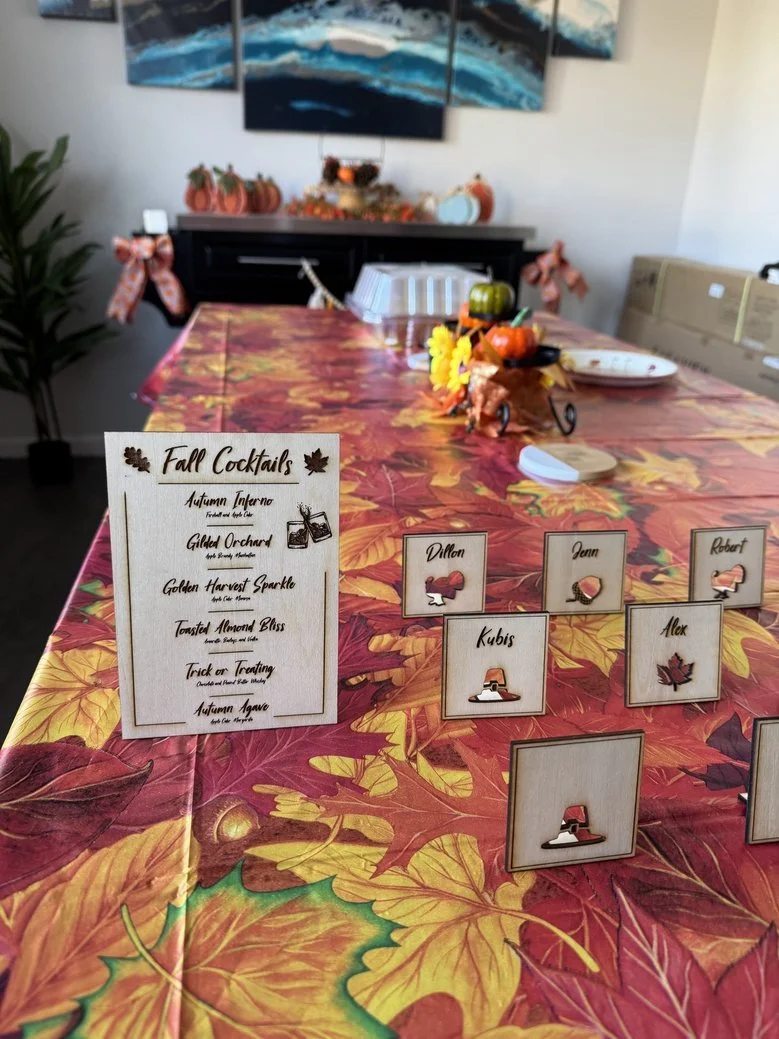 A decorated dining table with fall-themed tablecloth, small name cards with pumpkins, leaves, and Halloween symbols, and a menu titled 'Fall Cocktails' with autumn-inspired drinks listed.