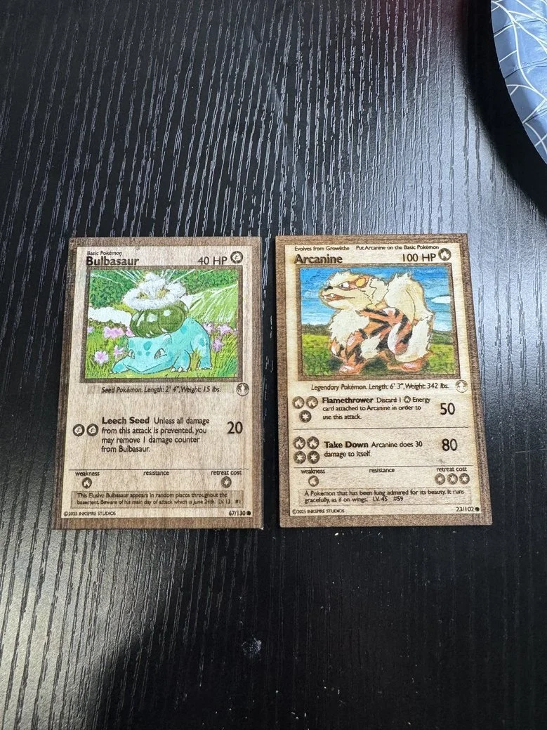Two Pokémon cards, Bulbasaur on the left and Arcanine on the right, placed on a dark wooden surface. Bulbasaur is a basic Pokémon with 40 HP, illustrated with a large plant bulb on its back, surrounded by greenery and flowers. Arcanine is a legendary