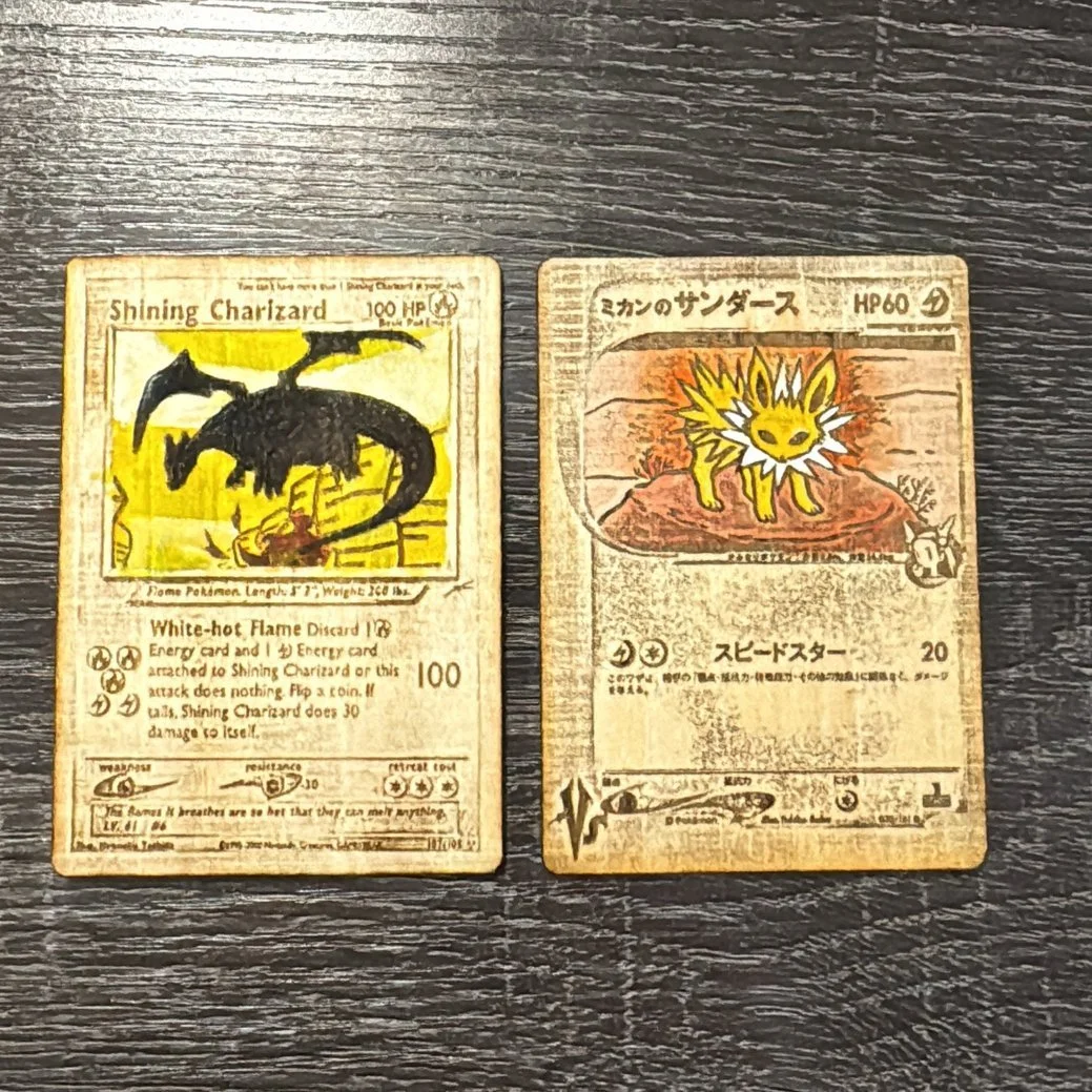 Two vintage Pokémon cards, one for Shining Charizard and one for Jolteon, laid on a dark wooden surface.