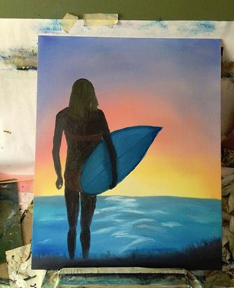 Silhouette of a woman holding a surfboard at sunset, standing on the beach with the ocean in the background.