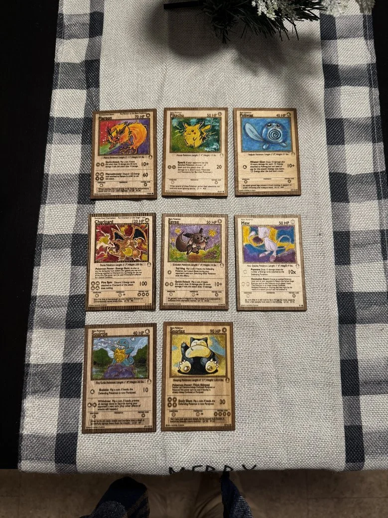 Nine vintage Pokémon trading cards arranged in three rows on a checkered tablecloth. The cards feature various Pokémon characters, including Flareon, Pikachu, Poliwhirl, Charizard, Eevee, Mew, Squirtle, and Snorlax.