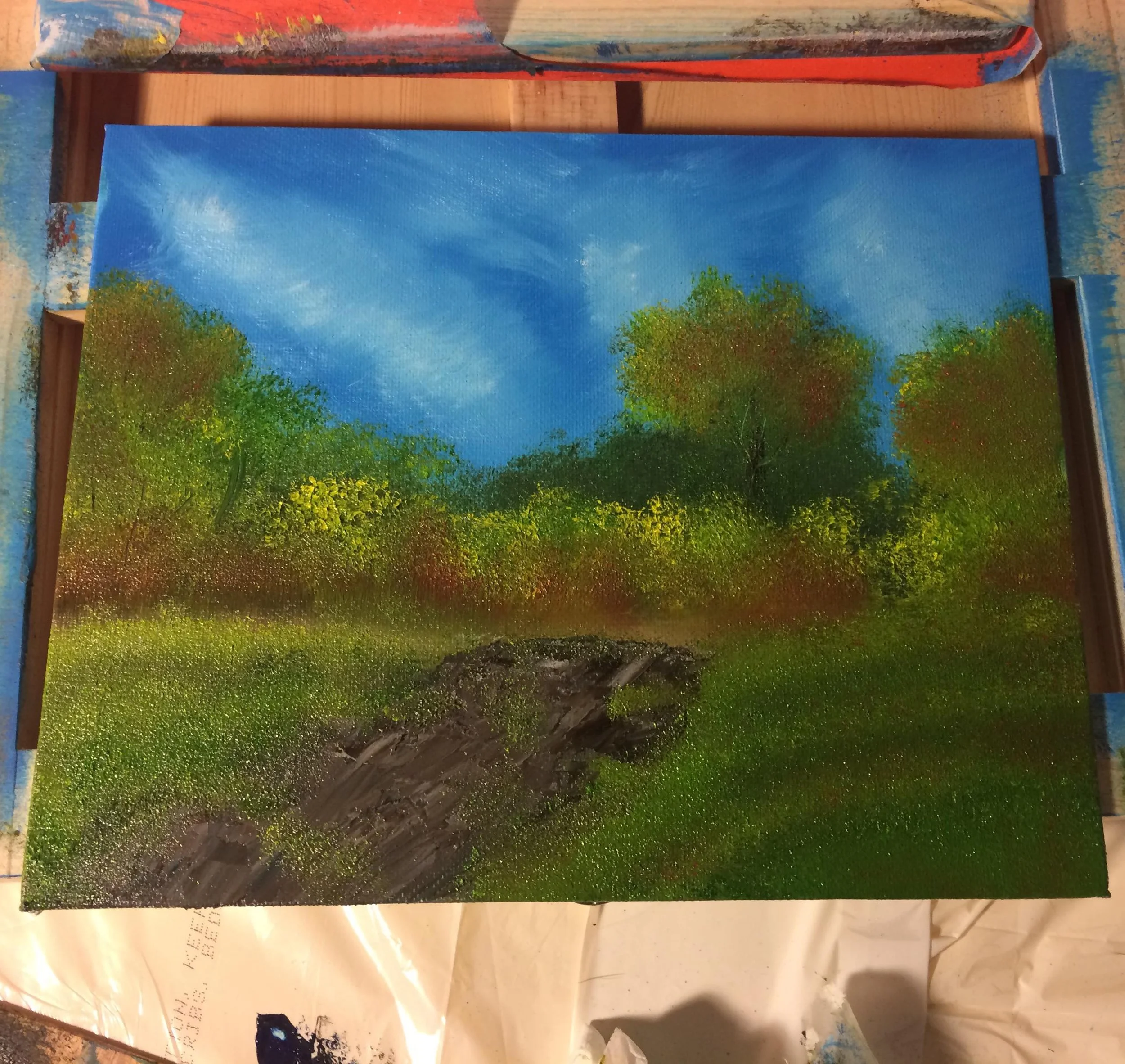 An oil painting of a natural landscape showing a grassy area with trees under a blue sky with wispy clouds, and a fallen log in the foreground.