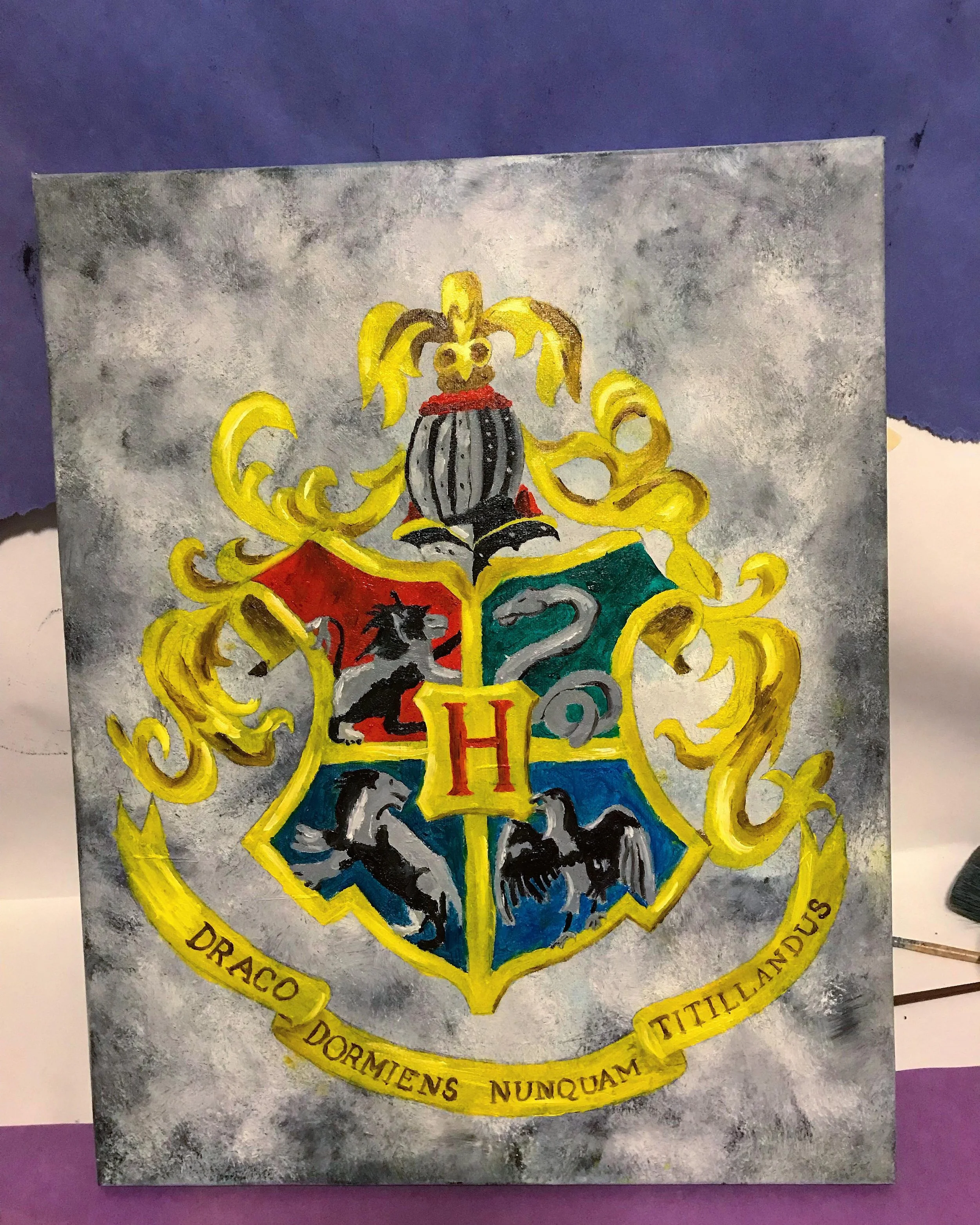 Artwork of the Hogwarts crest featuring the four houses with animals: lion, snake, raven, and badger, and the motto 'Draco Dormiens Nunquam Titillandus' on a yellow banner.