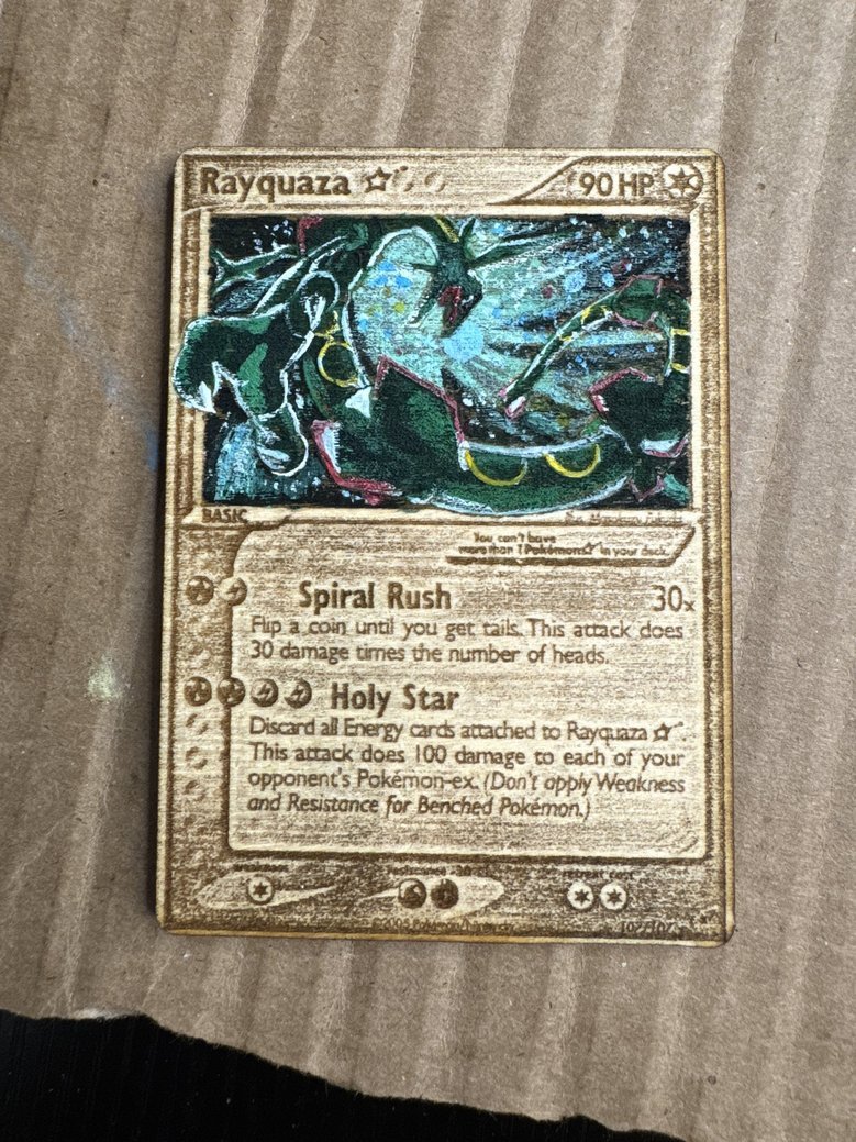 A hand-crafted Pokémon trading card for Rayquaza, illustrated with a detailed, colorful drawing of the dragon Pokémon. The card features moves Spiral Rush and Holy Star, with stats including 90 HP and effects described in text.
