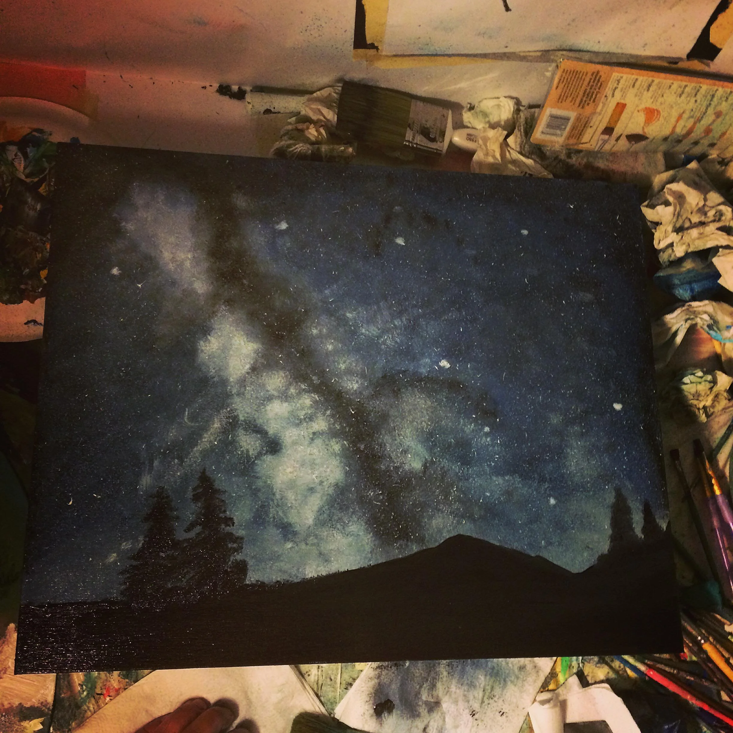 A painting of a night sky with stars and the Milky Way galaxy, silhouetted trees, and a hill in the foreground.